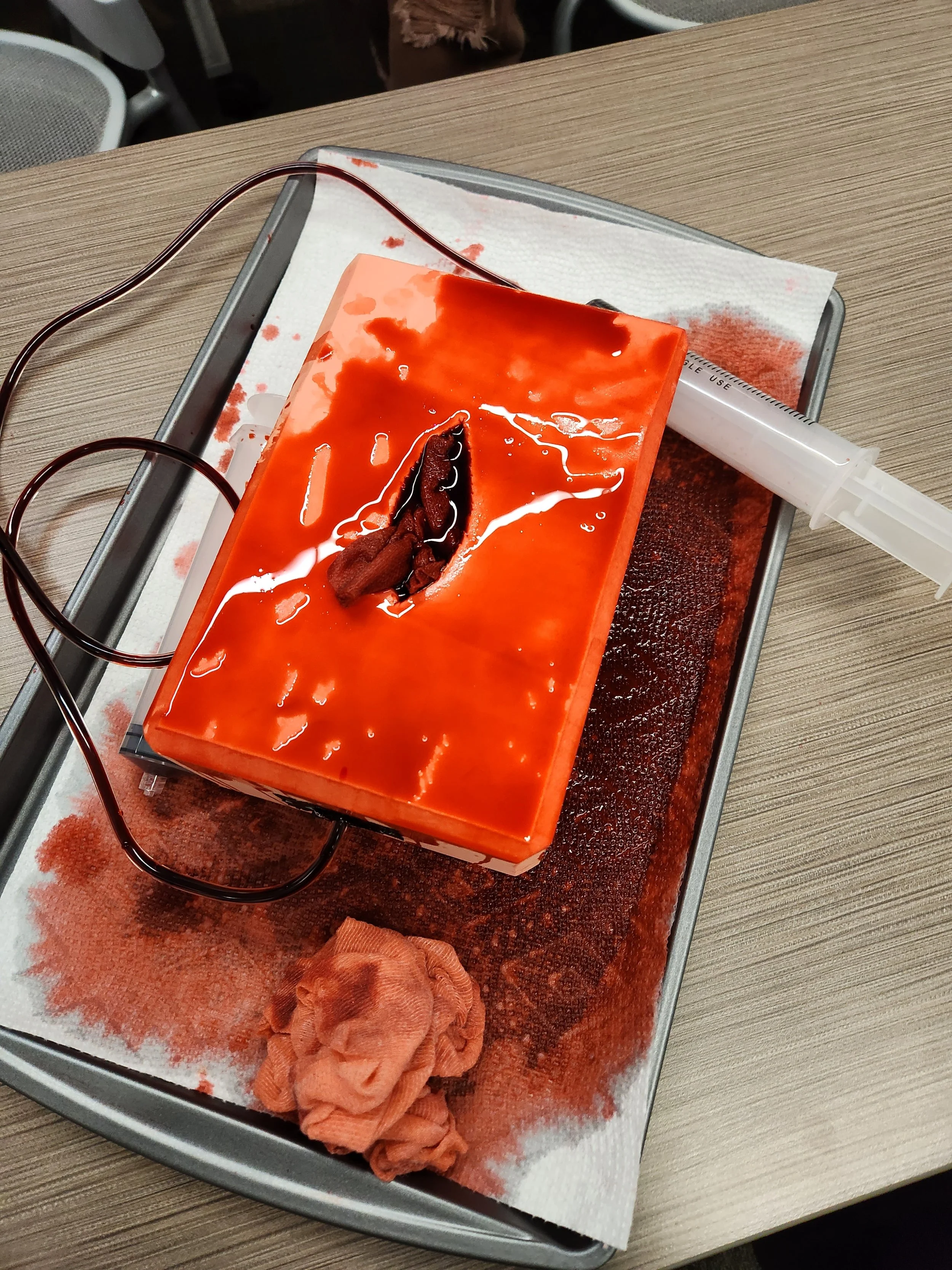 A wound packing simulator covered with fake blood used for training students on packing junctional areas with gauze.