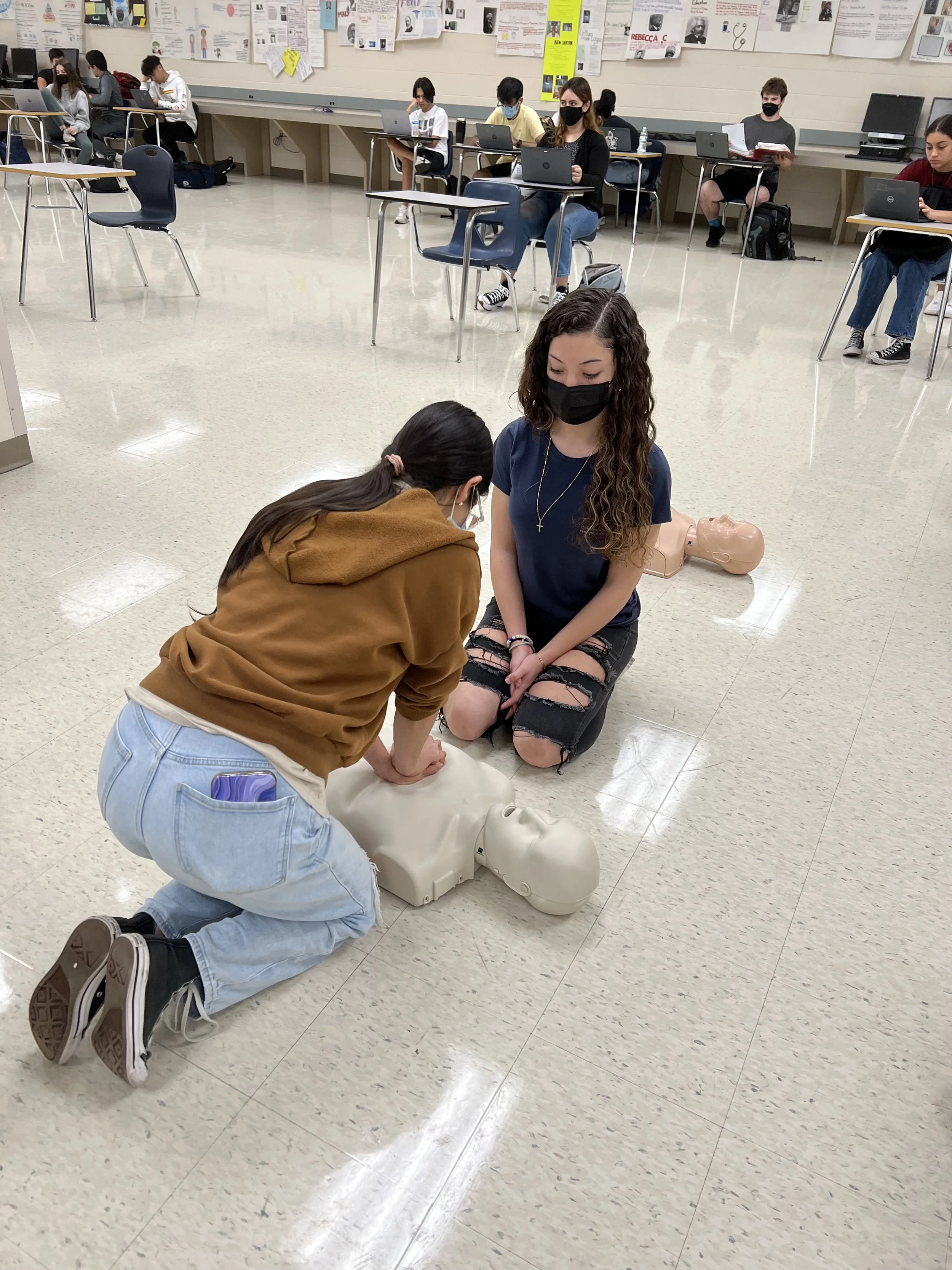 Students practicing CPR on mannequins in a classroom