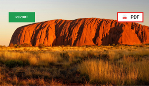 A large, reddish-brown rock formation, likely Uluru, with dry grassland in the foreground and a clear sky in the background.