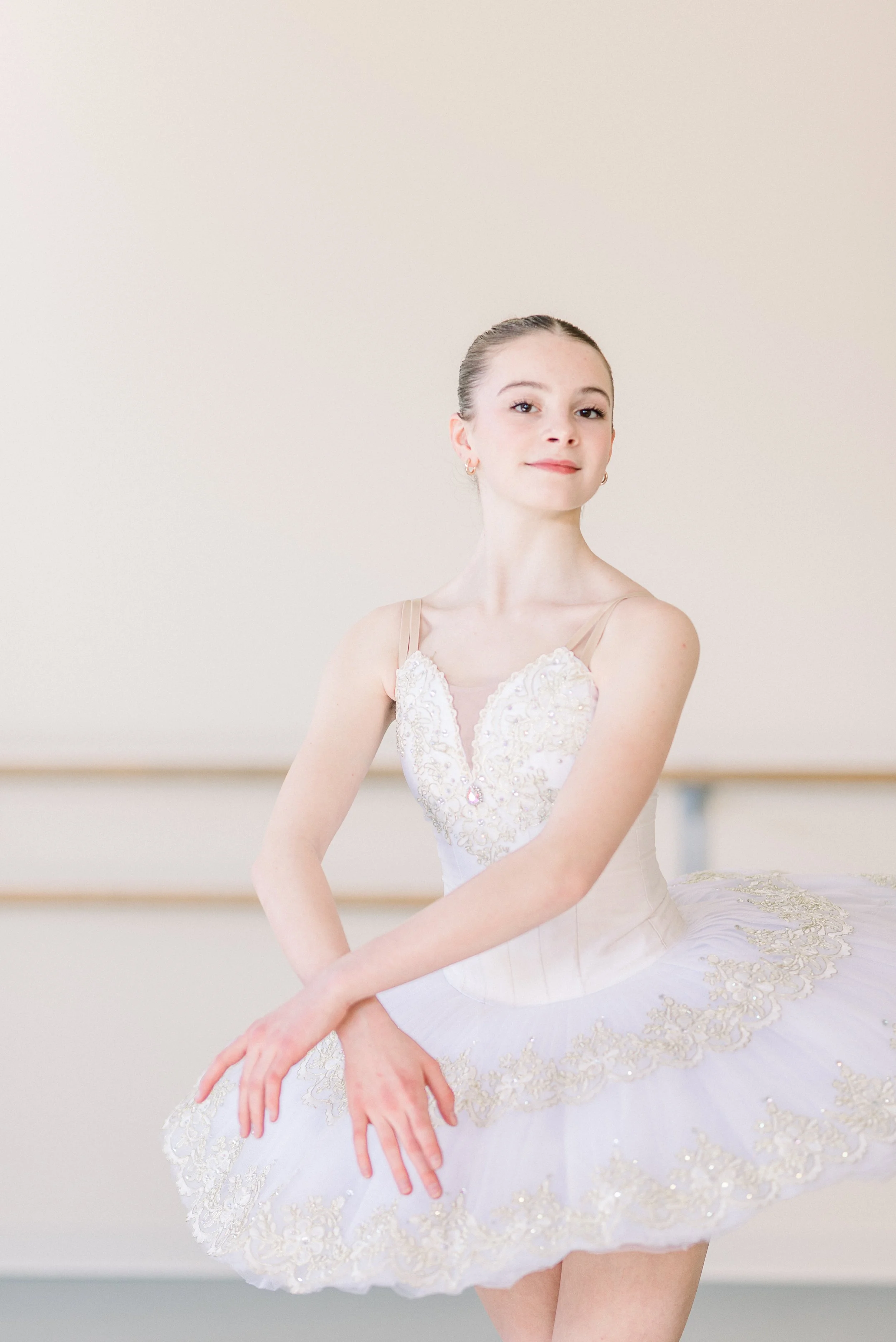 Ballet dancer in a white tutu with gold embroidery, standing in a dance studio.