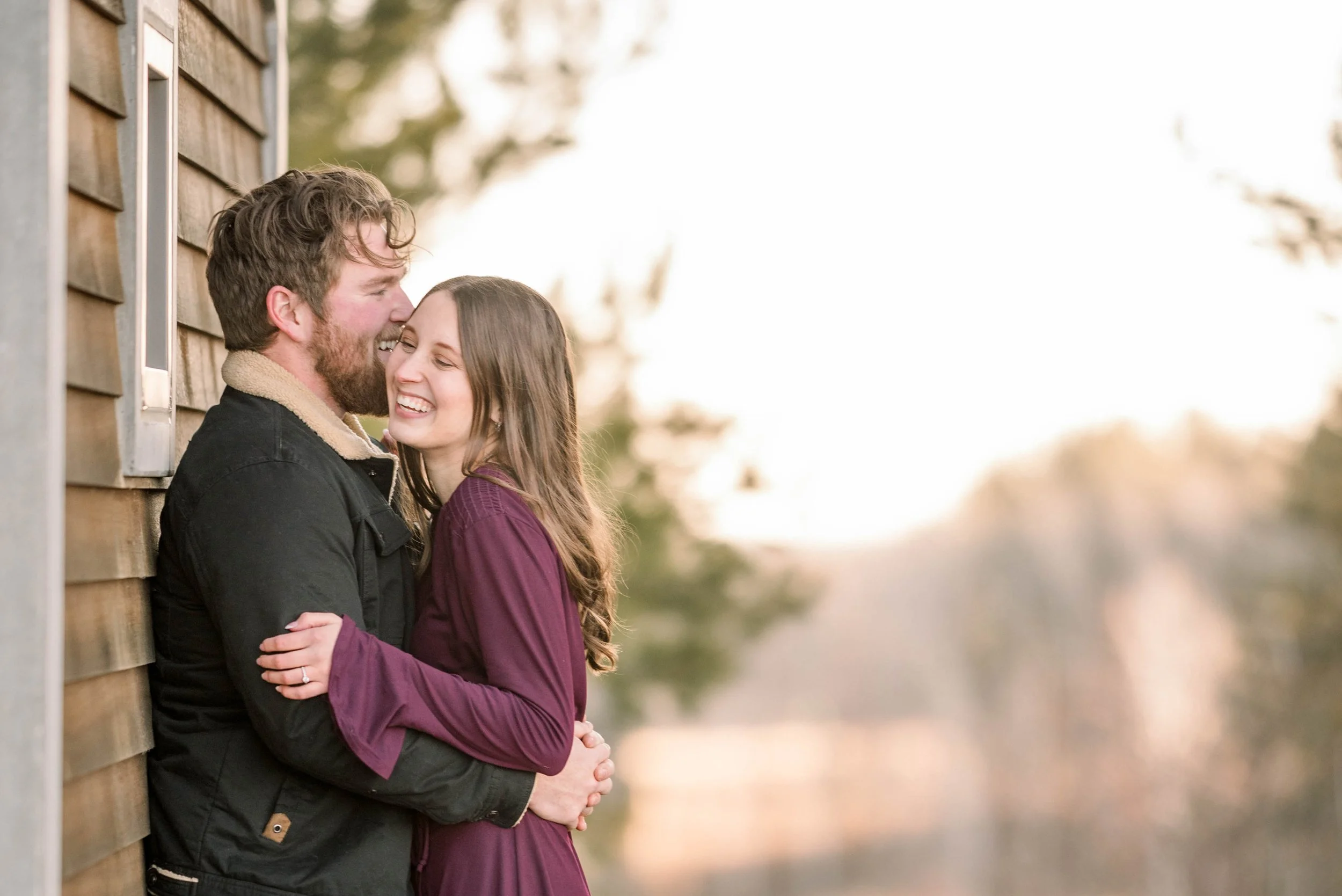 A happy couple embracing outdoors near a wooden building during sunset.