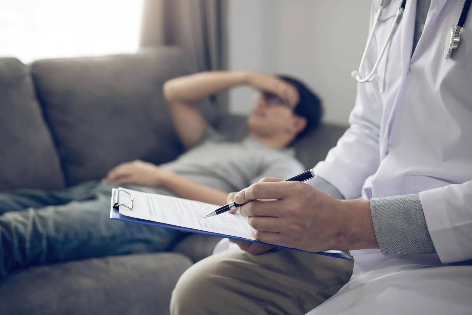 doctor-writing-on-a-clipboard,-with-a-patient-lying-on-a-couch-in-the-background