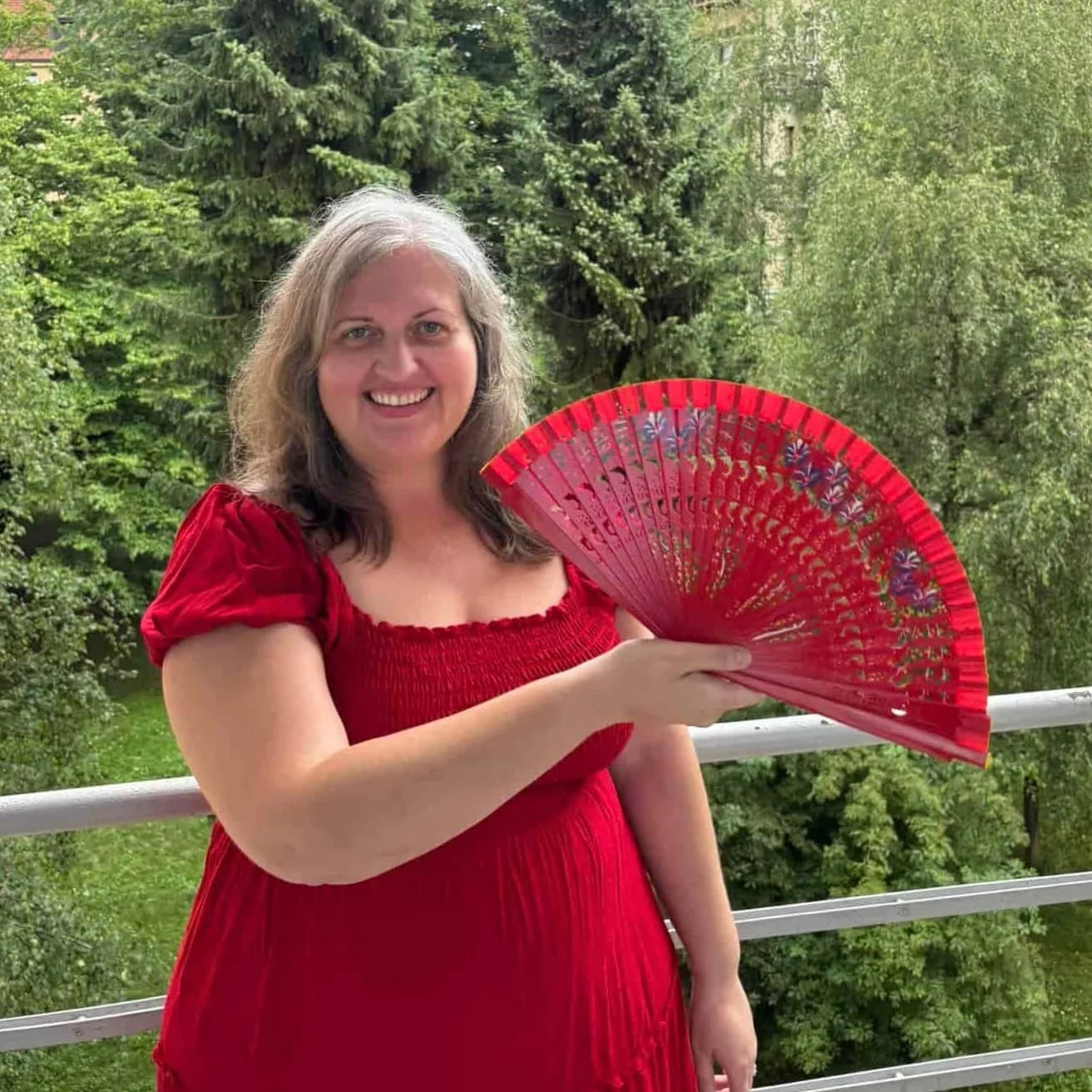 Karina Ramirez, coach and somatic facilitator, in a red dres holding a hand fan