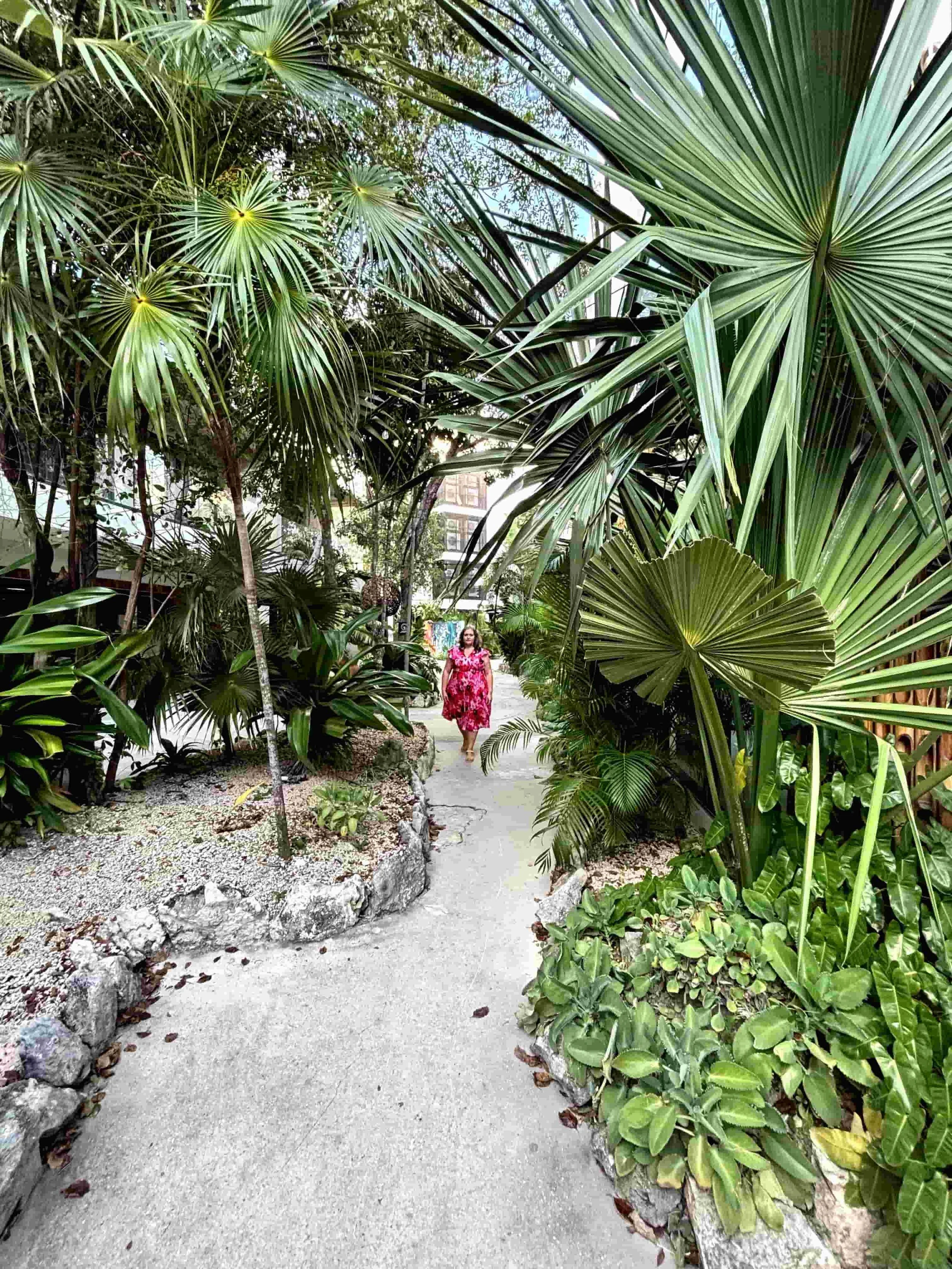 Karina Ramirez, Somatic Facilitator and Connection Coach, in a tropical garden setting, wearing a pink floral dress and soft smile