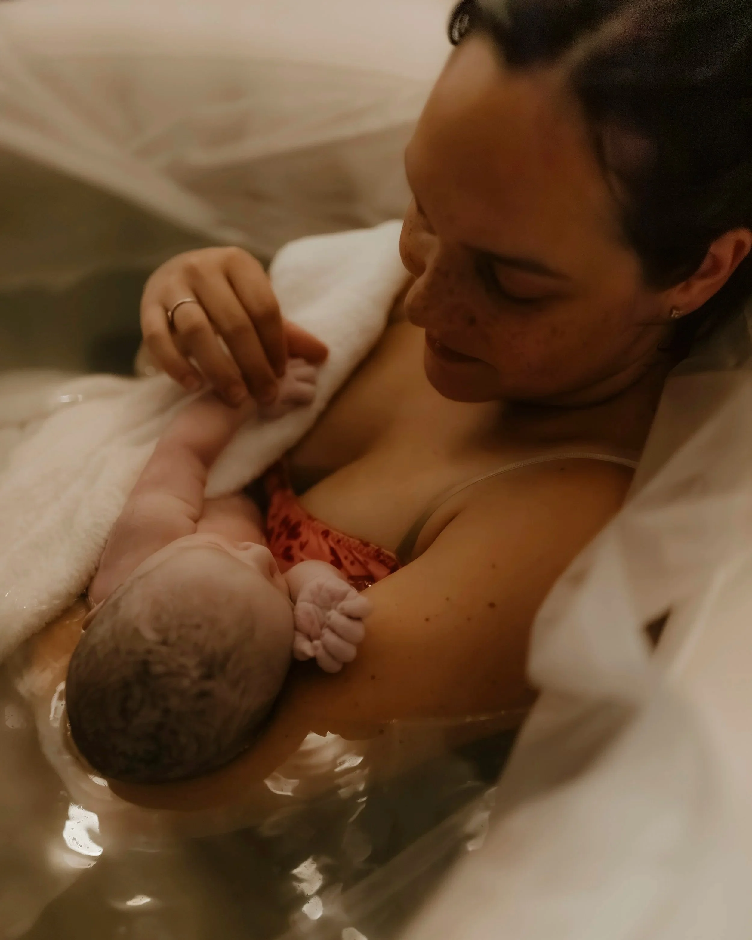 Mother lying in bed holding newborn baby under a white towel.
