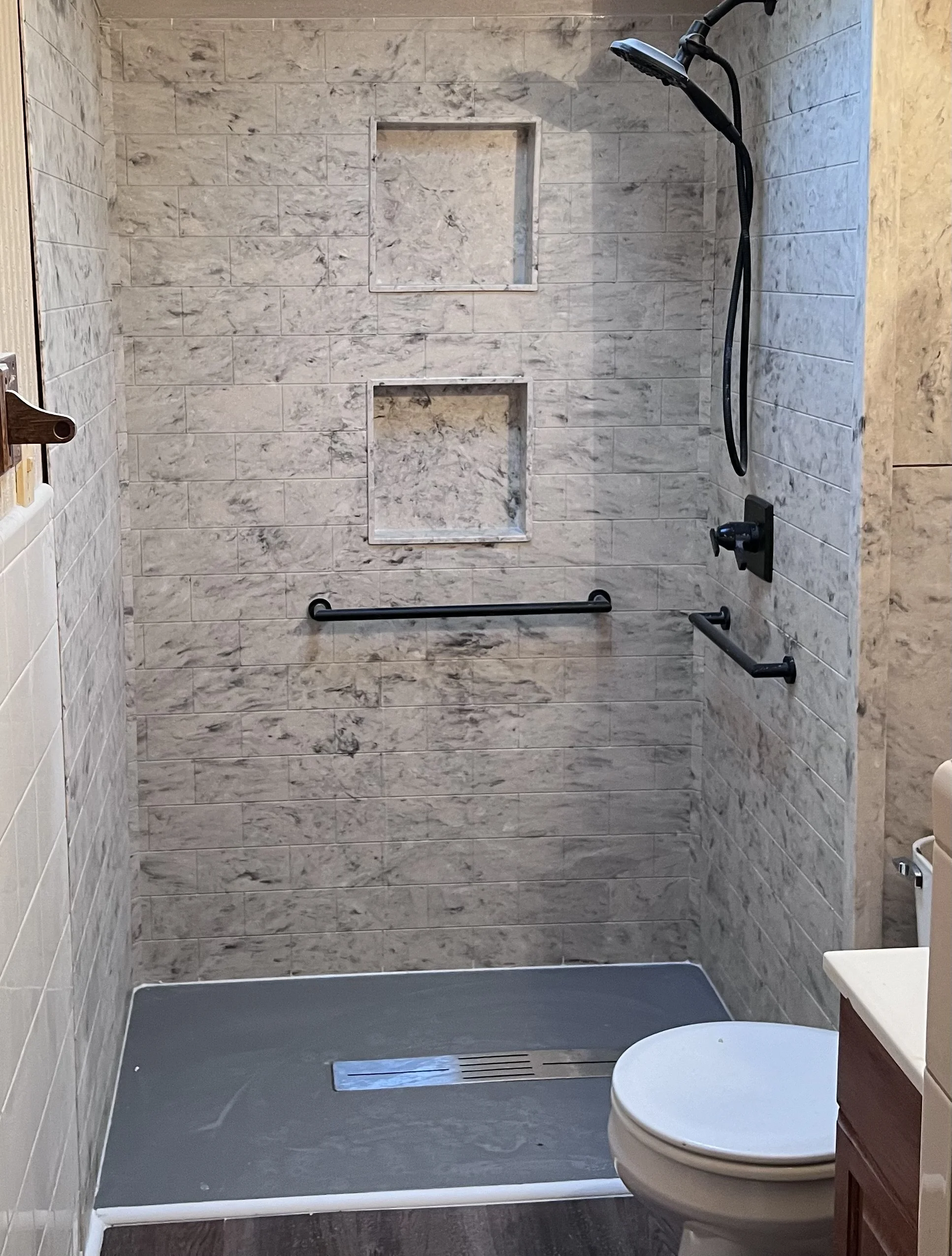 Bathroom with walk-in shower, gray marble tiles, grab bars, and handheld showerhead.