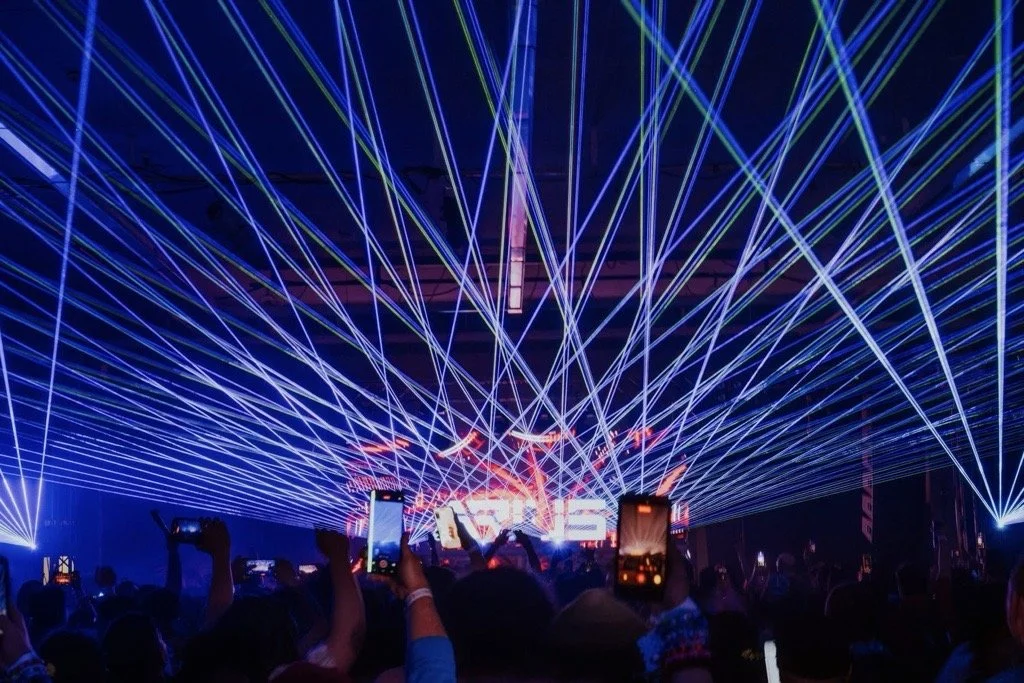 Crowd at a concert with laser light show and a large digital display.