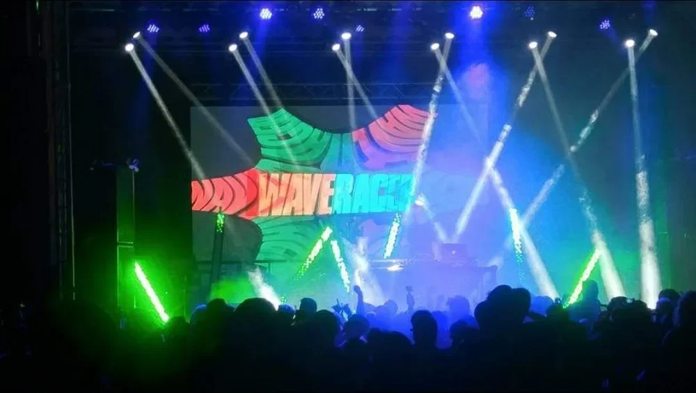 Concert stage with colorful lights and a large LED screen displaying the words 'DANNY WERACE' in bright colors, with a crowd of people watching.