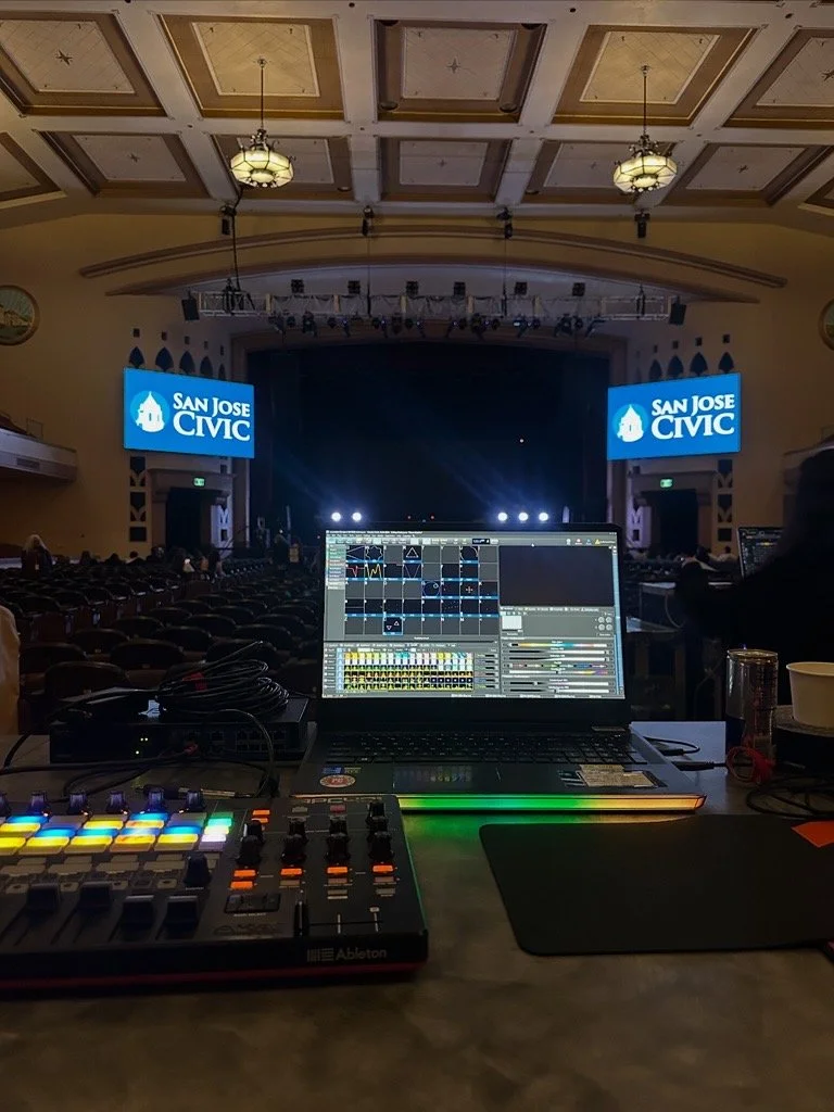 A view of a stage with two screens displaying 'San Jose CIVIC' logos, set up in an auditorium, with a sound mixing and lighting control setup in the foreground.