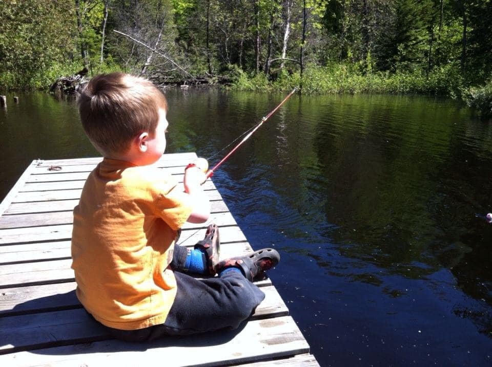 Young boy sitting on a dock and fishing in a lake.