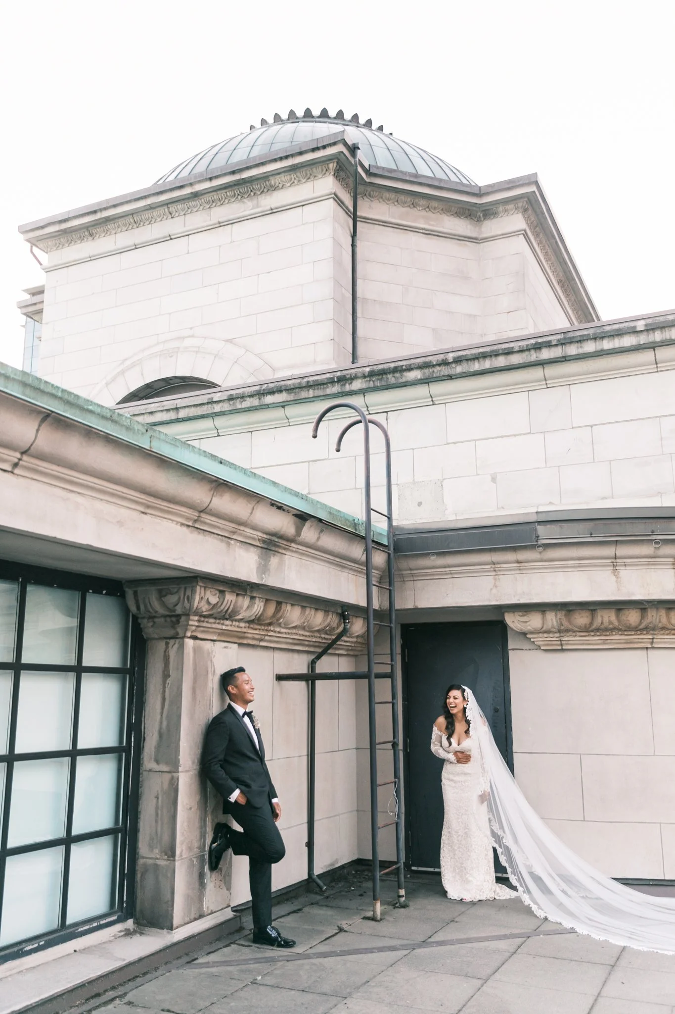 Bride and groom in elegant attire on a rooftop with a domed building Vancouver Art Gallery in the background. www.alextownsend.ca