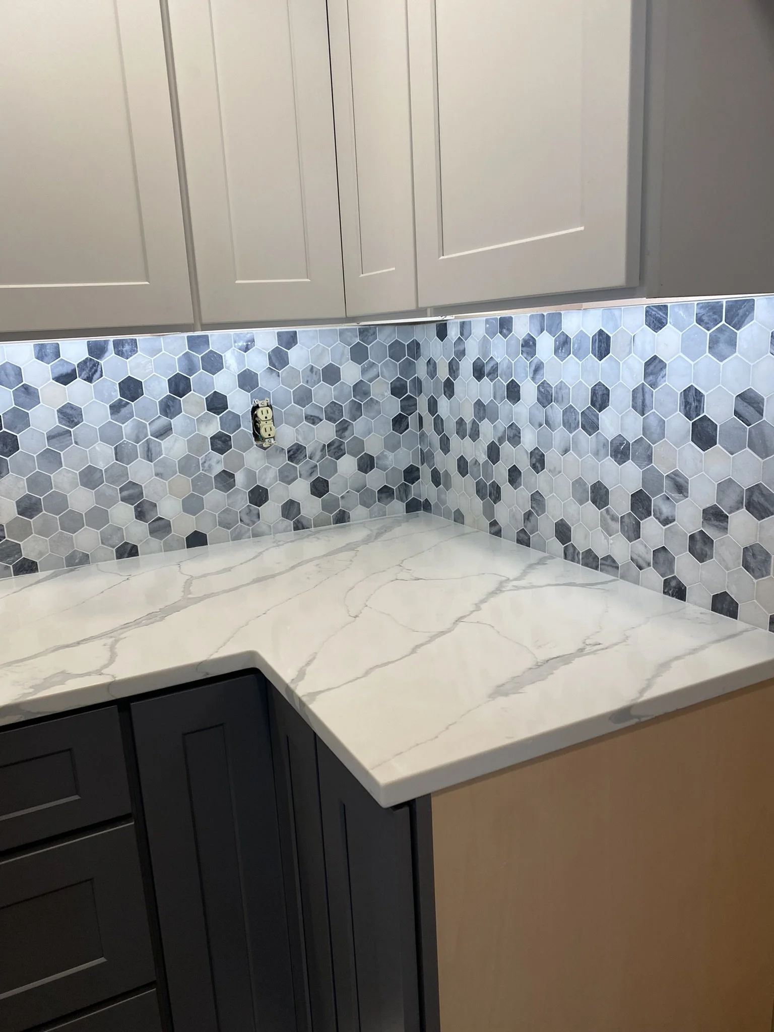 Kitchen corner with white marble countertop, gray upper cabinets, and a gray hexagon tile backsplash.