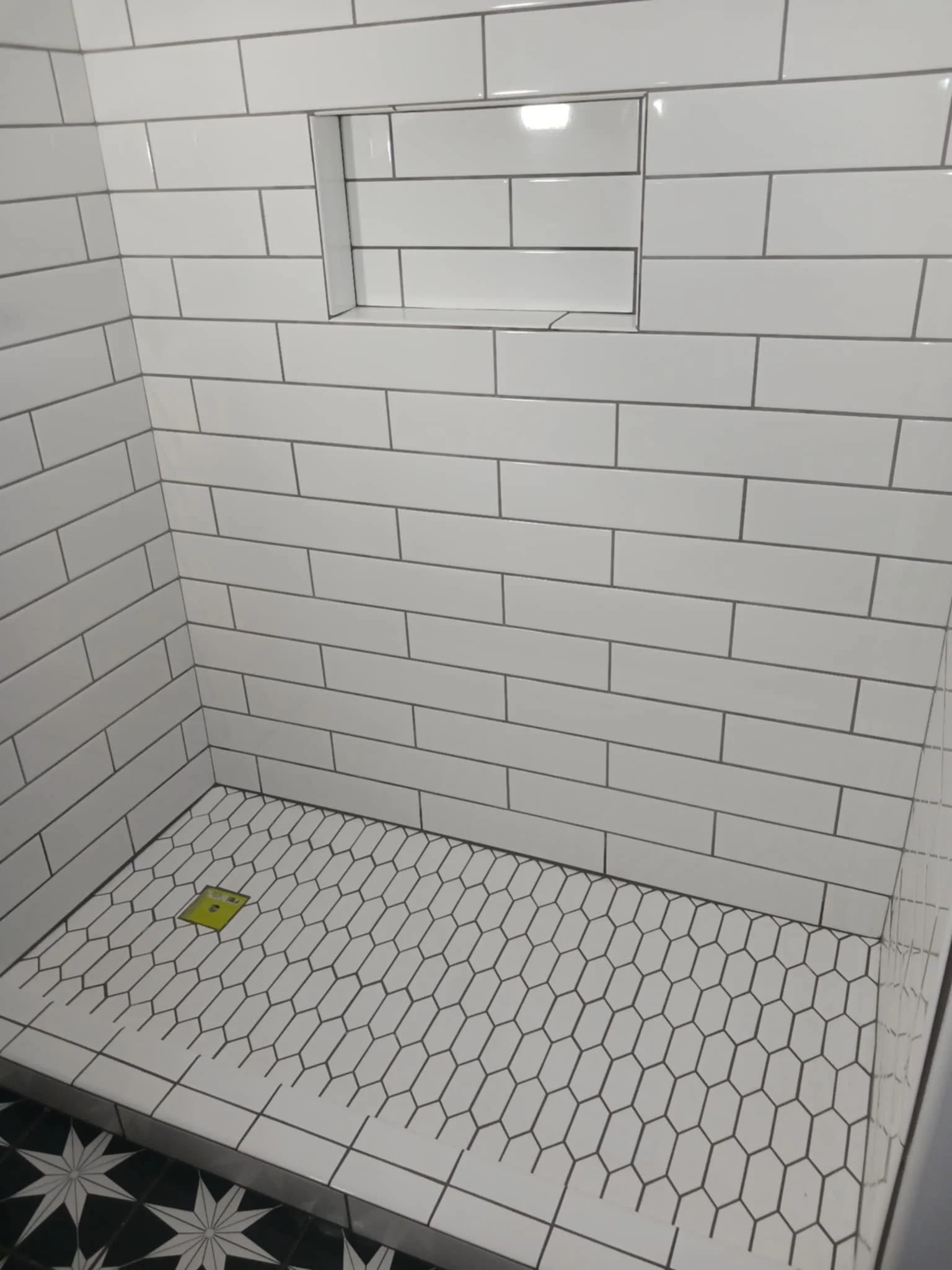 Empty shower with white subway tiles, hexagon floor tiles, and a built-in niche.