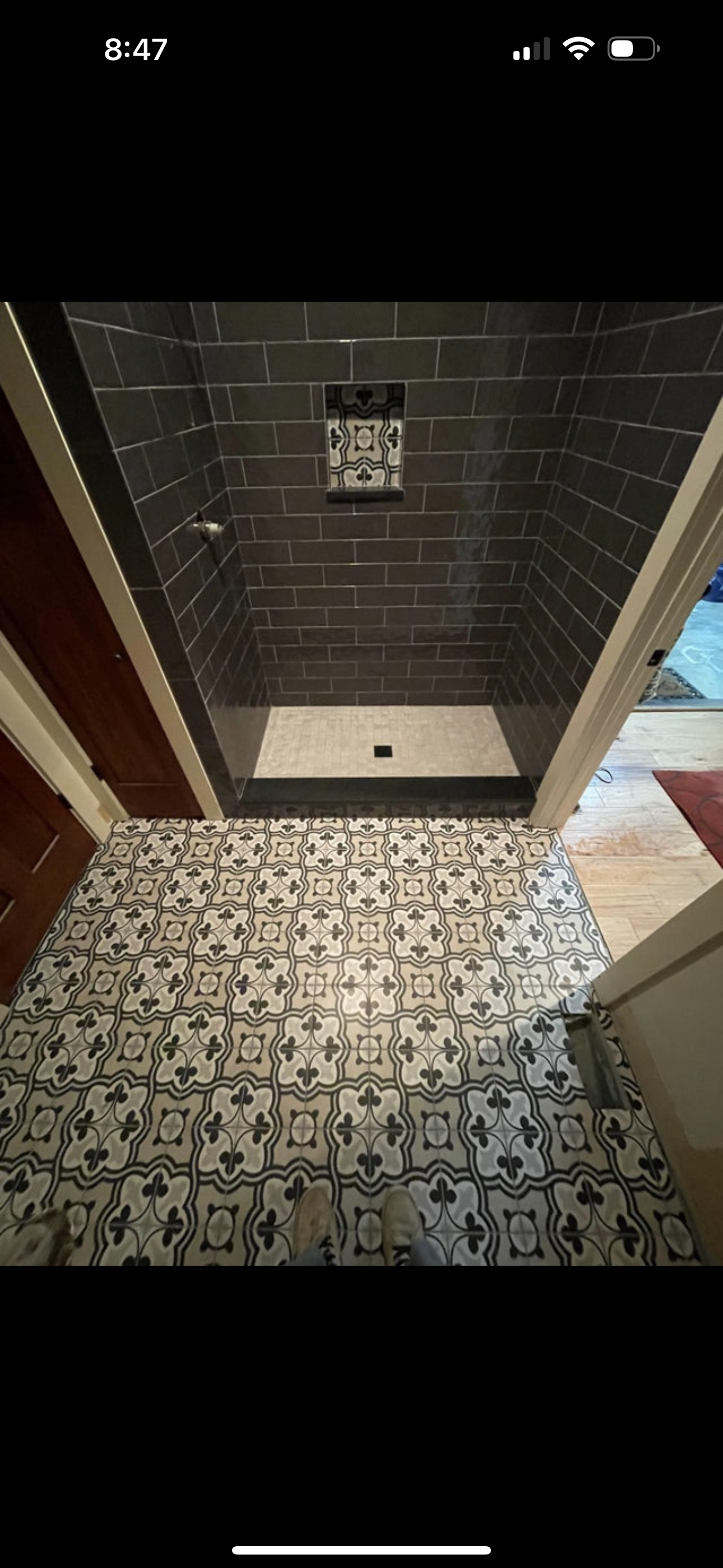 A tiled bathroom with a patterned floor and a walk-in shower with dark gray subway tiles and a decorative tile accent.
