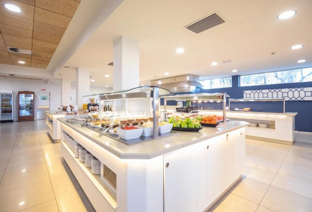 Buffet area with plates of fruits, desserts, and breakfast items in a bright, modern dining space.