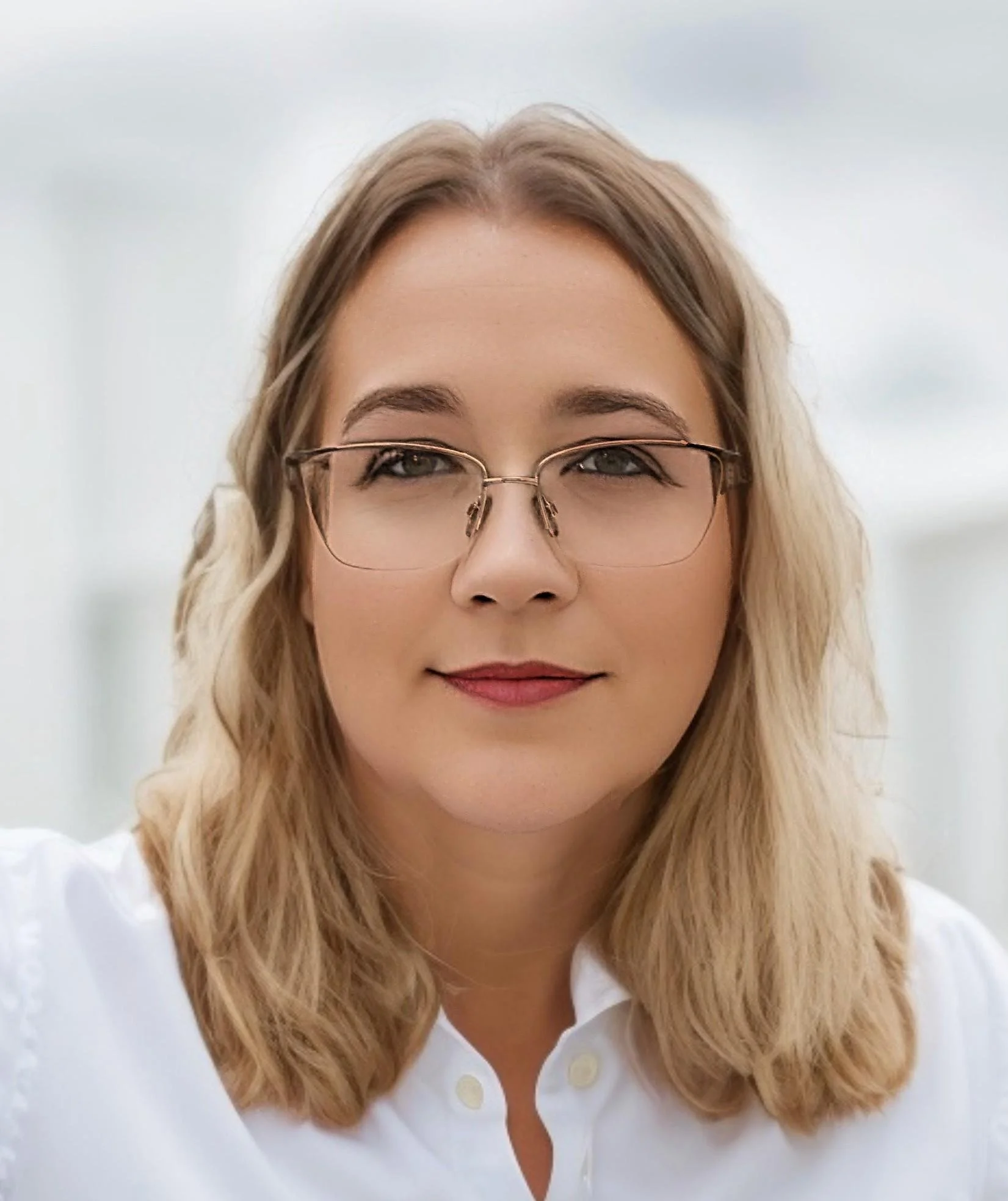 Close-up of a woman with blond wavy hair, wearing glasses and a white blouse, smiling against a white background.