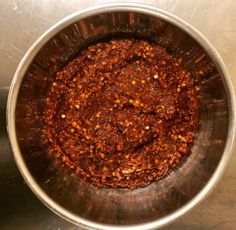 A metal bowl filled with a dark, chunky paste that appears to be a chili or spice mixture. Adobo spice blend. Cayenne. Spicy paste. Hot. Latin American.