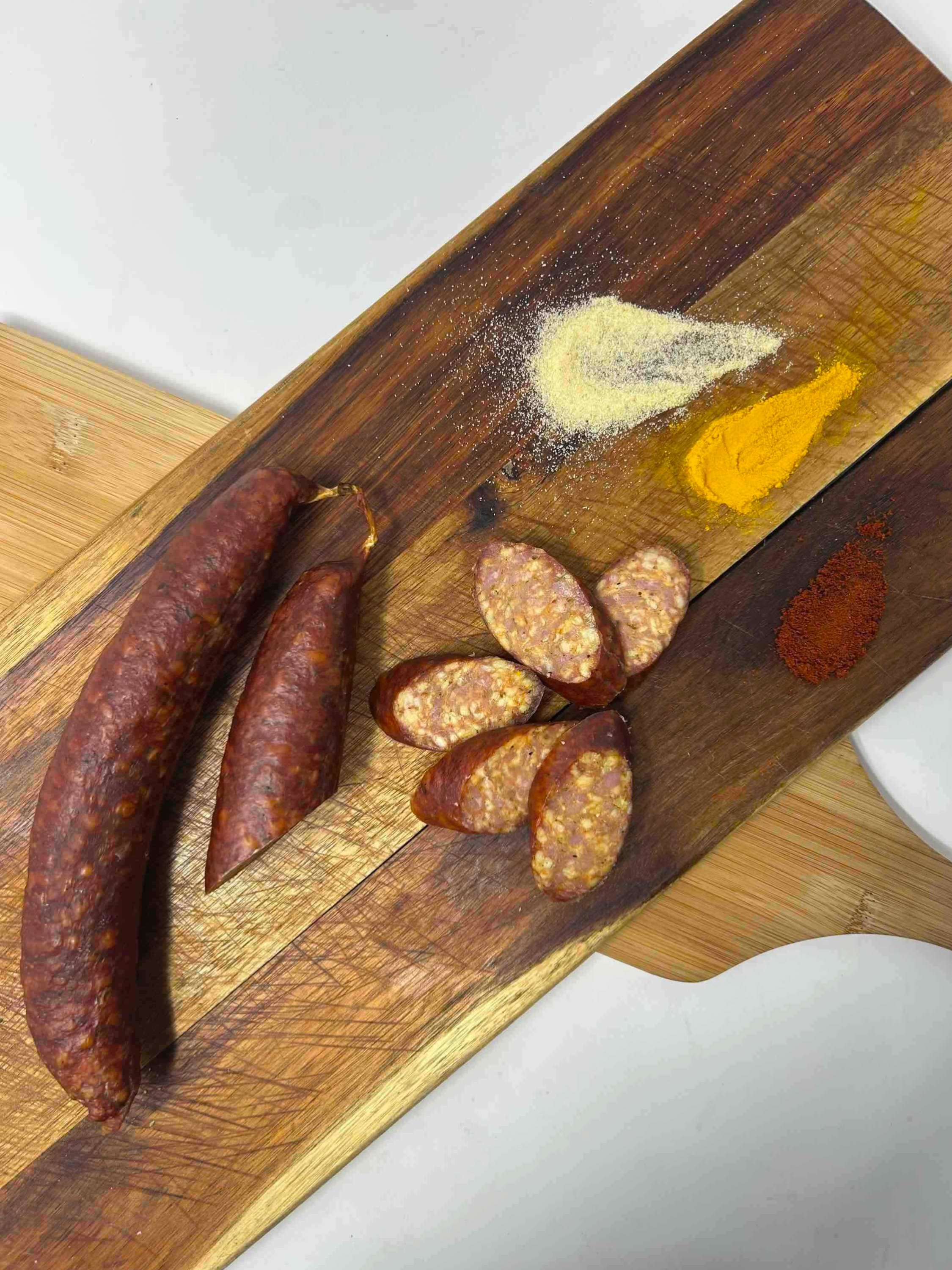 Sausages and sliced sausage links on a wooden cutting board with spices such as turmeric, paprika, and garlic powder