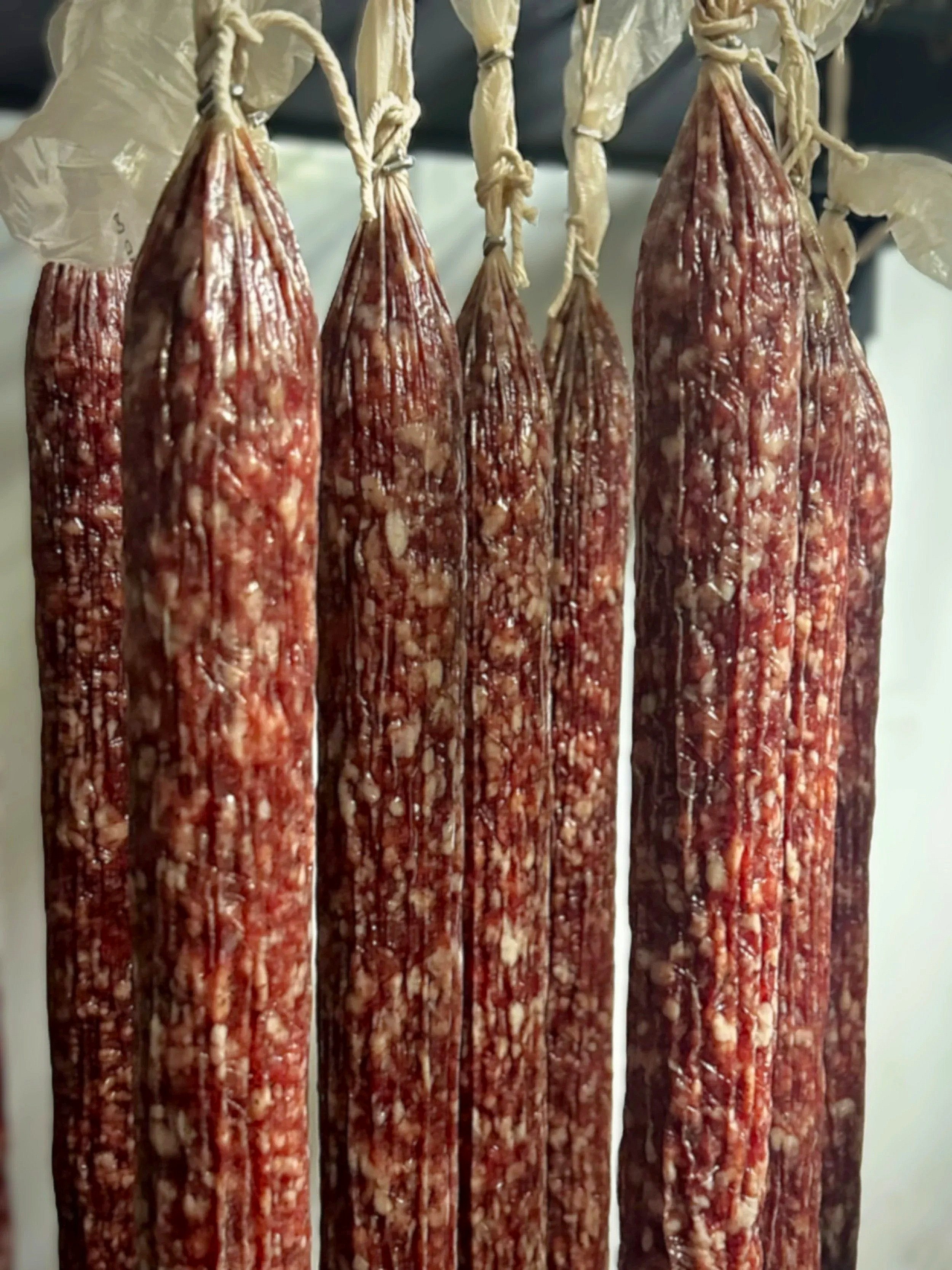 Five cured salami hanging by ropes in a row, drying or smoking.