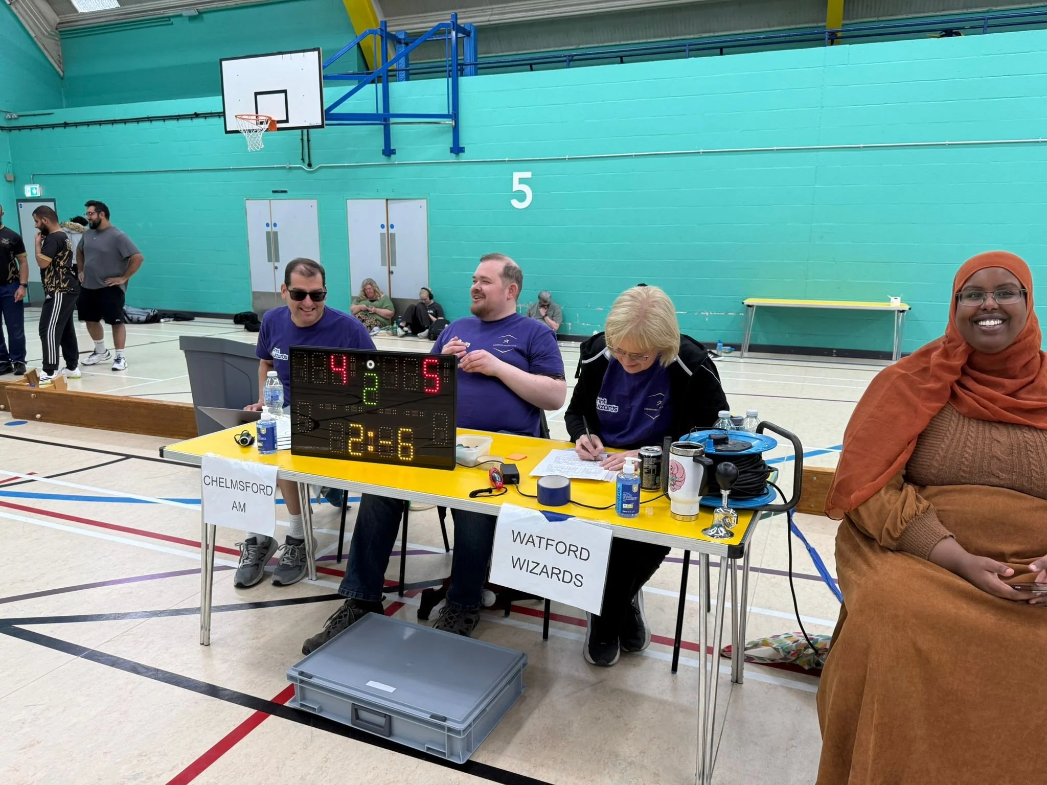  Officials seated at the scoring table during a goalball match. A digital scoreboard shows Chelmsford leading Watford Wizards 5–4 with 2 minutes and 36 seconds remaining.  