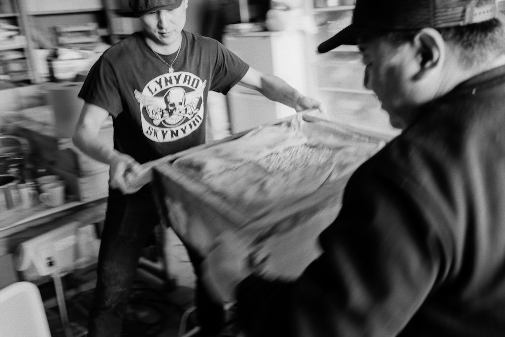 Deux personnes manipulent une grande caisse en bois dans un entrepôt.