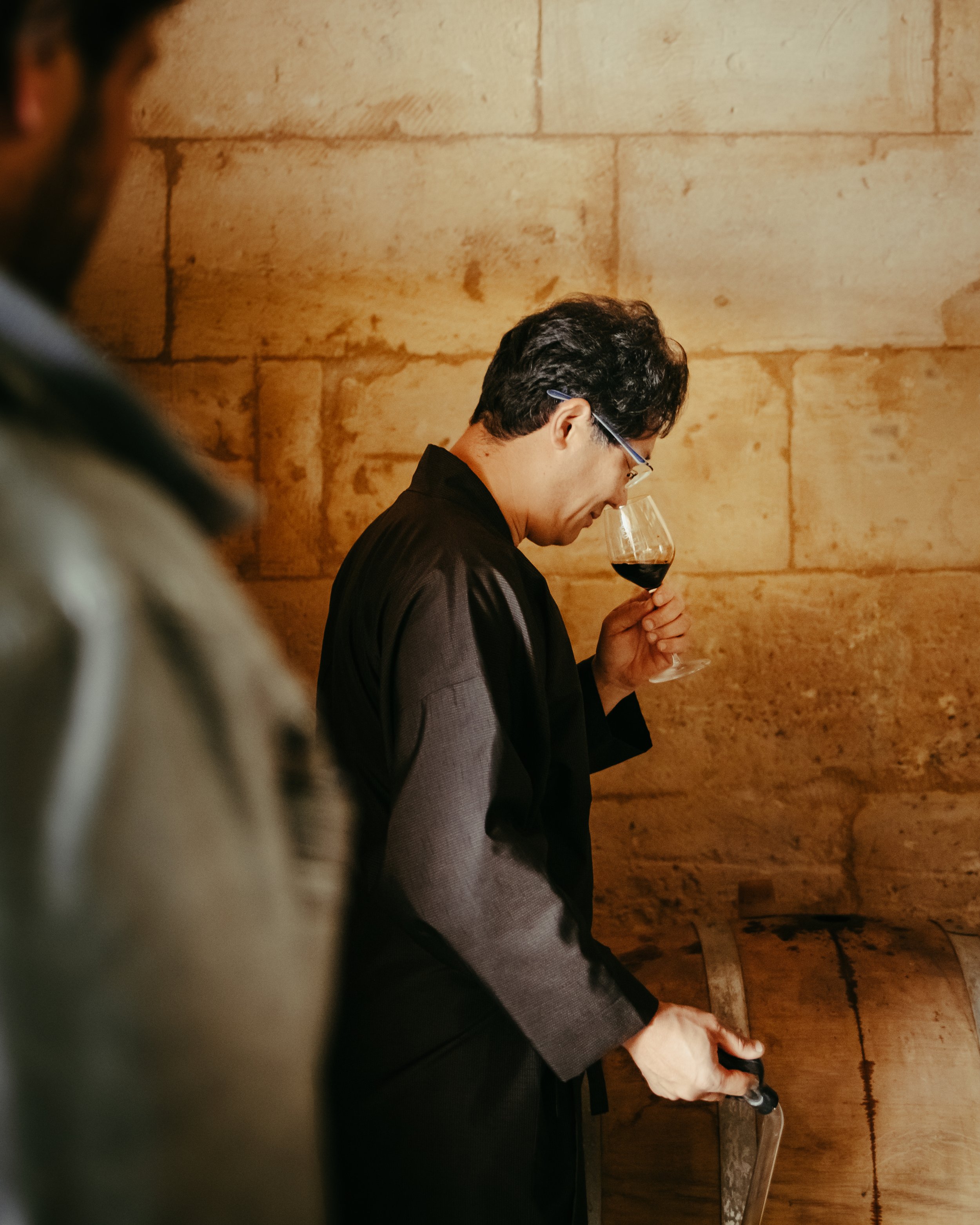 Un homme en costume traditionnel japonais portant des lunettes hume un verre de sauce soja de la maison shinko