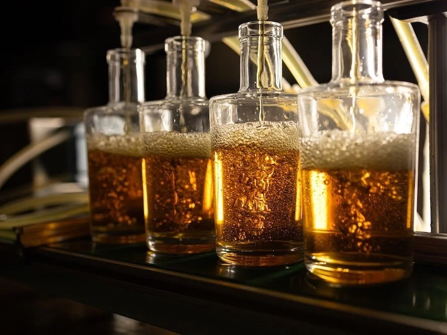 Bouteilles en verre contenant une boisson gazeuse dorée, suspendues à un système de distribution, avec du liquide qui s'écoule dans les bouteilles.