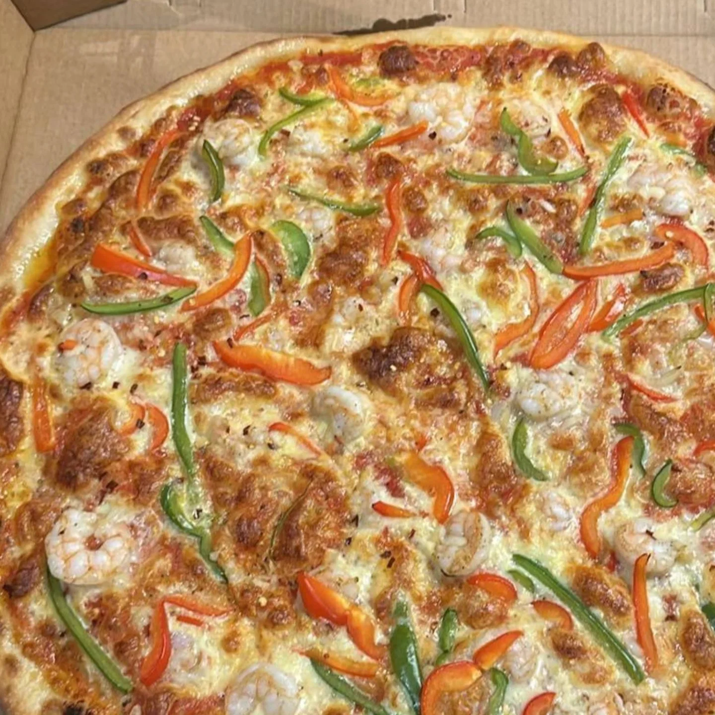 A pizza topped with cheese, green and red bell peppers, shrimp, and sausage slices.
