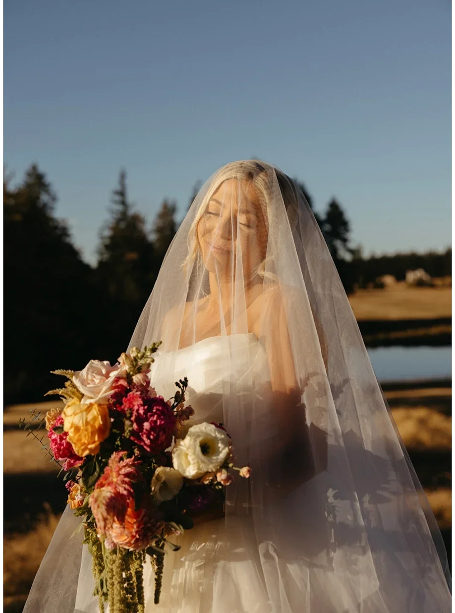 Bride in white holding bridal bouquet with roses, peonies, lisianthus, draping amaranth, celosia and other wedding flowers in Portland Oregon