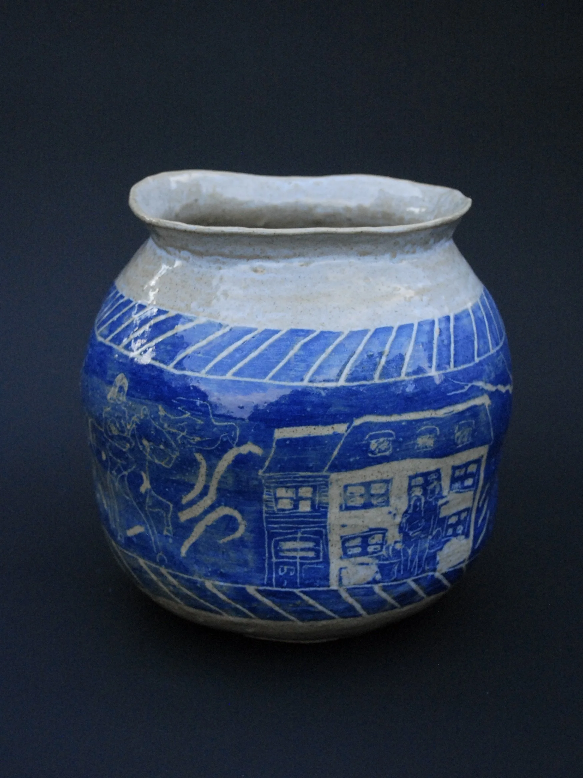 A greek inspired stoneware pot with hand-etched blue designs against a warm, earthy tone. It has a unique and slightly irregular shape adding to the rustic appeal