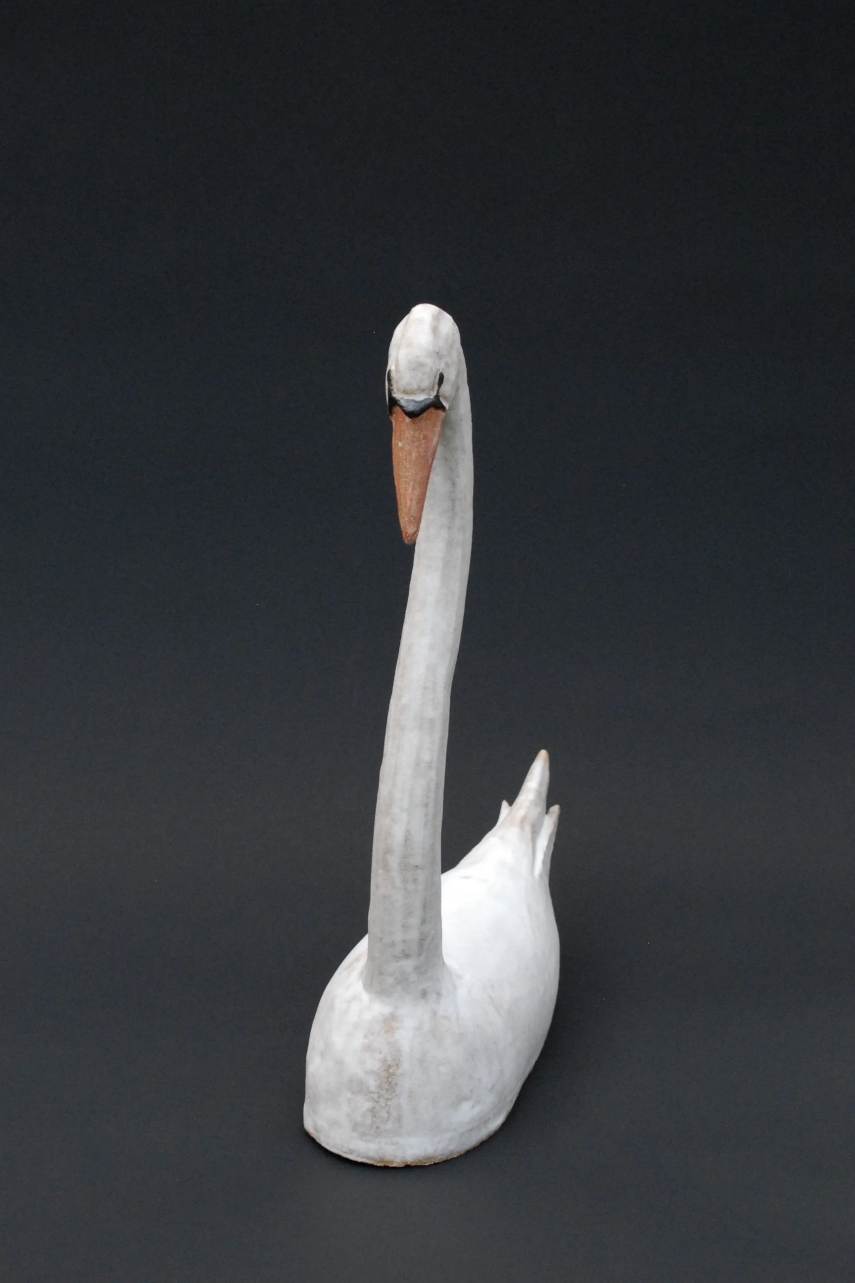 Image shows a large ceramic swan, covered in a white glaze with an orange beak. The swan has an particularly long neck in proportion to its body
