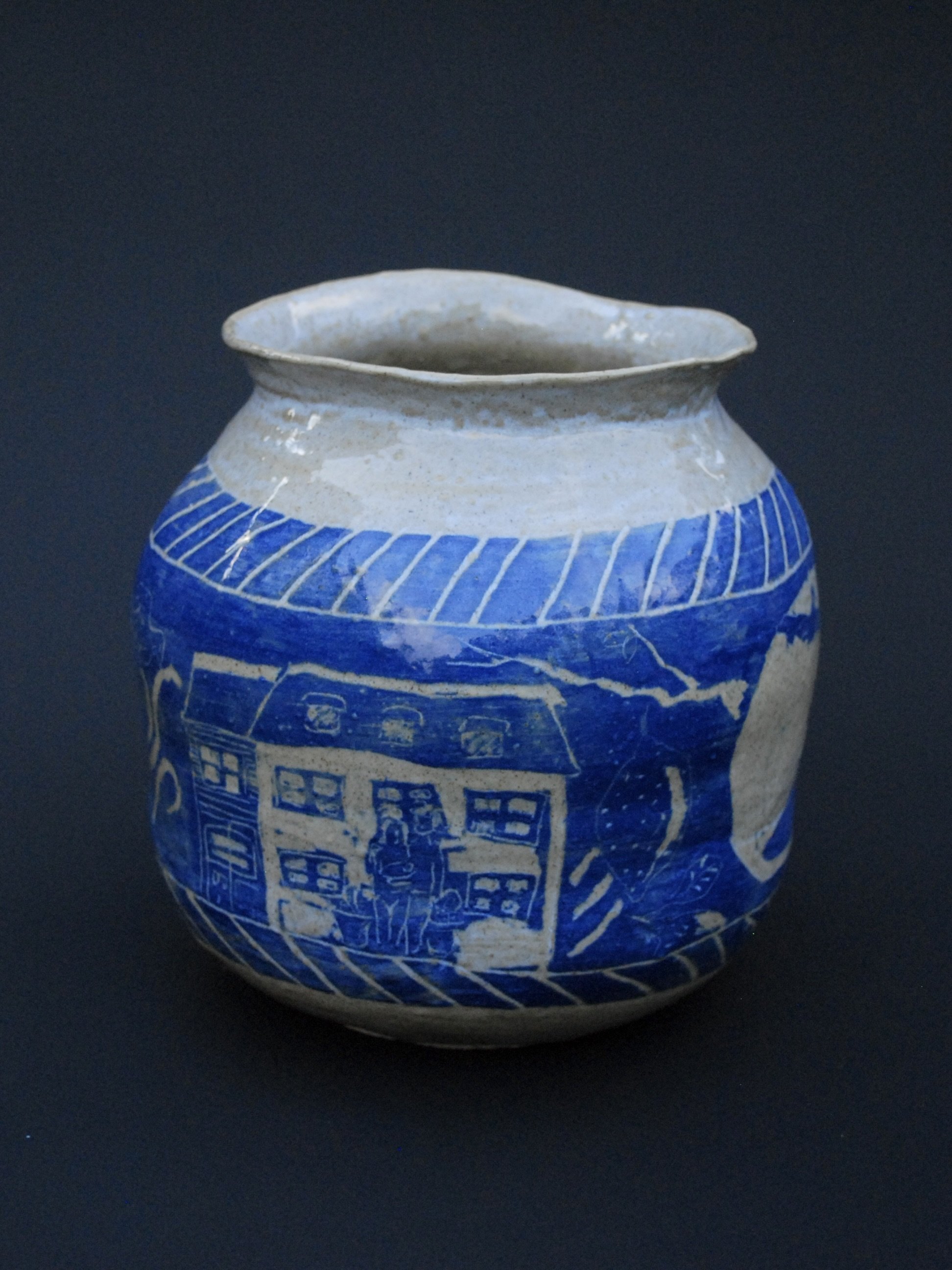 A greek inspired stoneware pot with hand-etched blue designs against a warm, earthy tone. It has a unique and slightly irregular shape adding to the rustic appeal