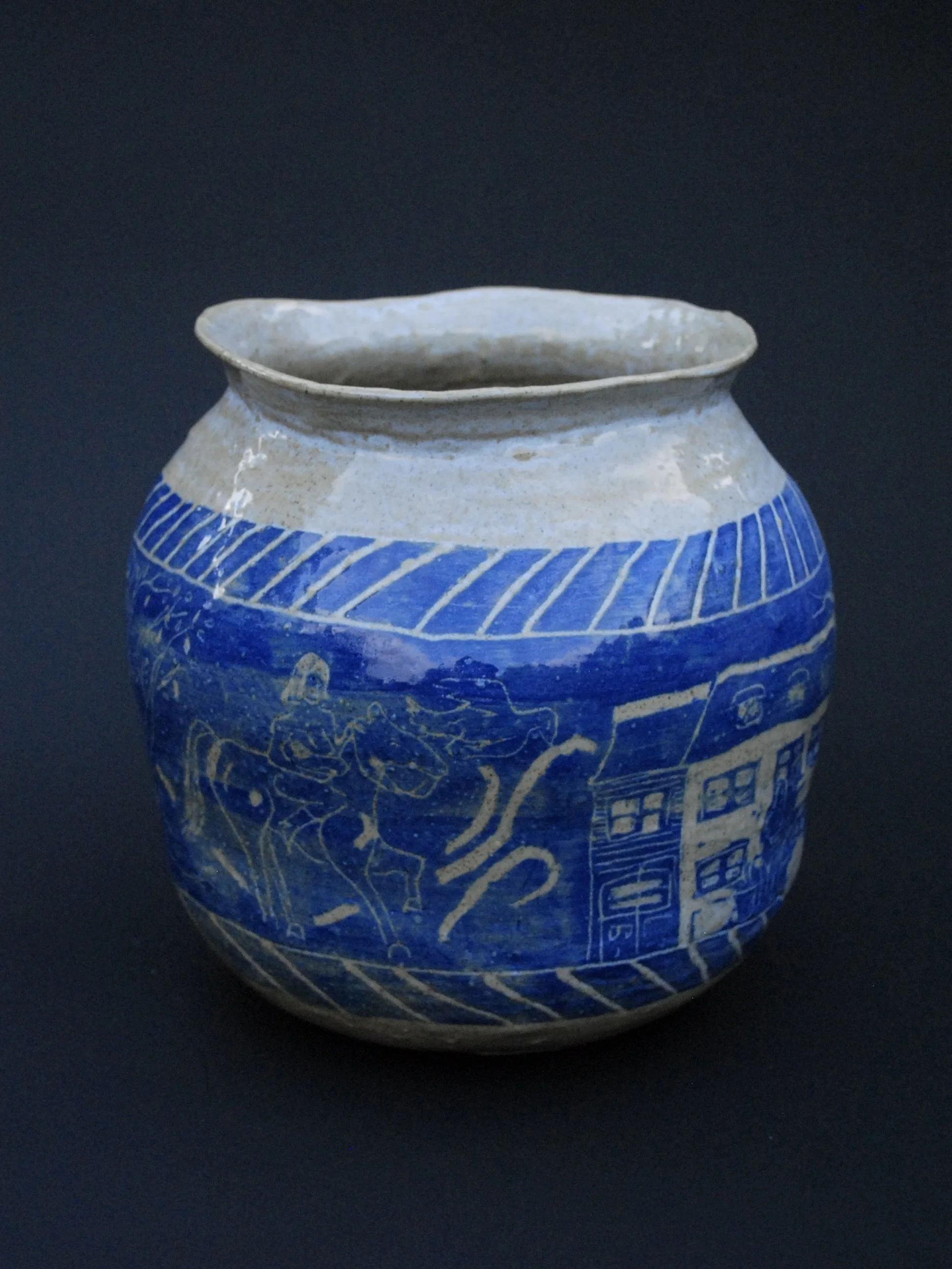 A greek inspired stoneware pot with hand-etched blue designs against a warm, earthy tone. It has a unique and slightly irregular shape adding to the rustic appeal