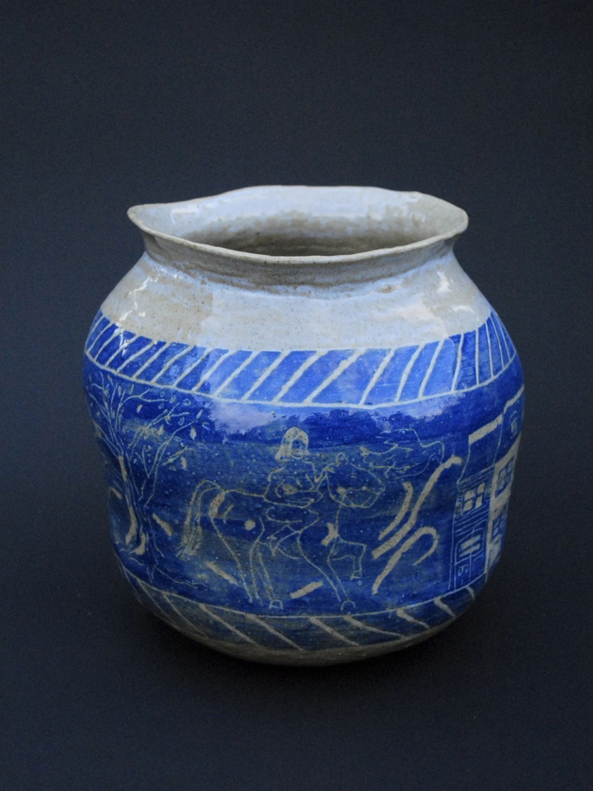 A greek inspired stoneware pot with hand-etched blue designs against a warm, earthy tone. It has a unique and slightly irregular shape adding to the rustic appeal