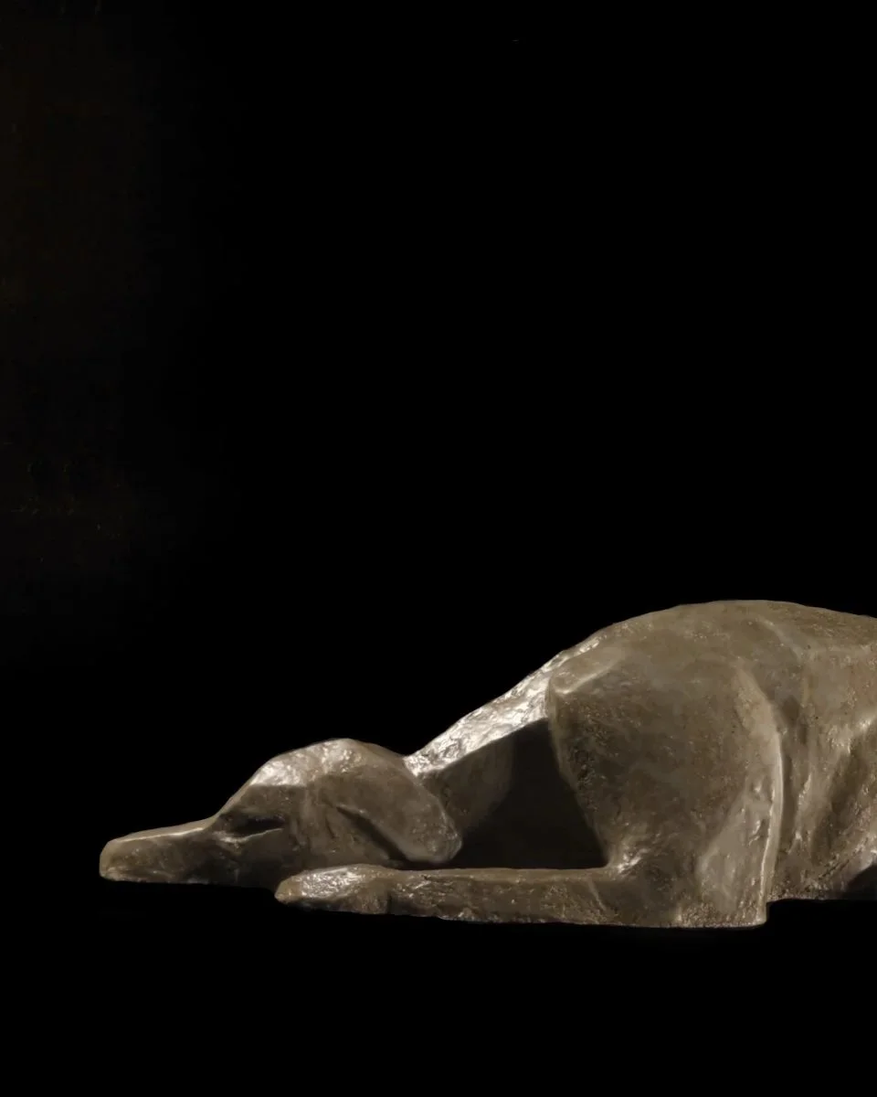 The Hound, ceramic sculpture of a sleeping hound lying with its head resting on its paws, side view on black