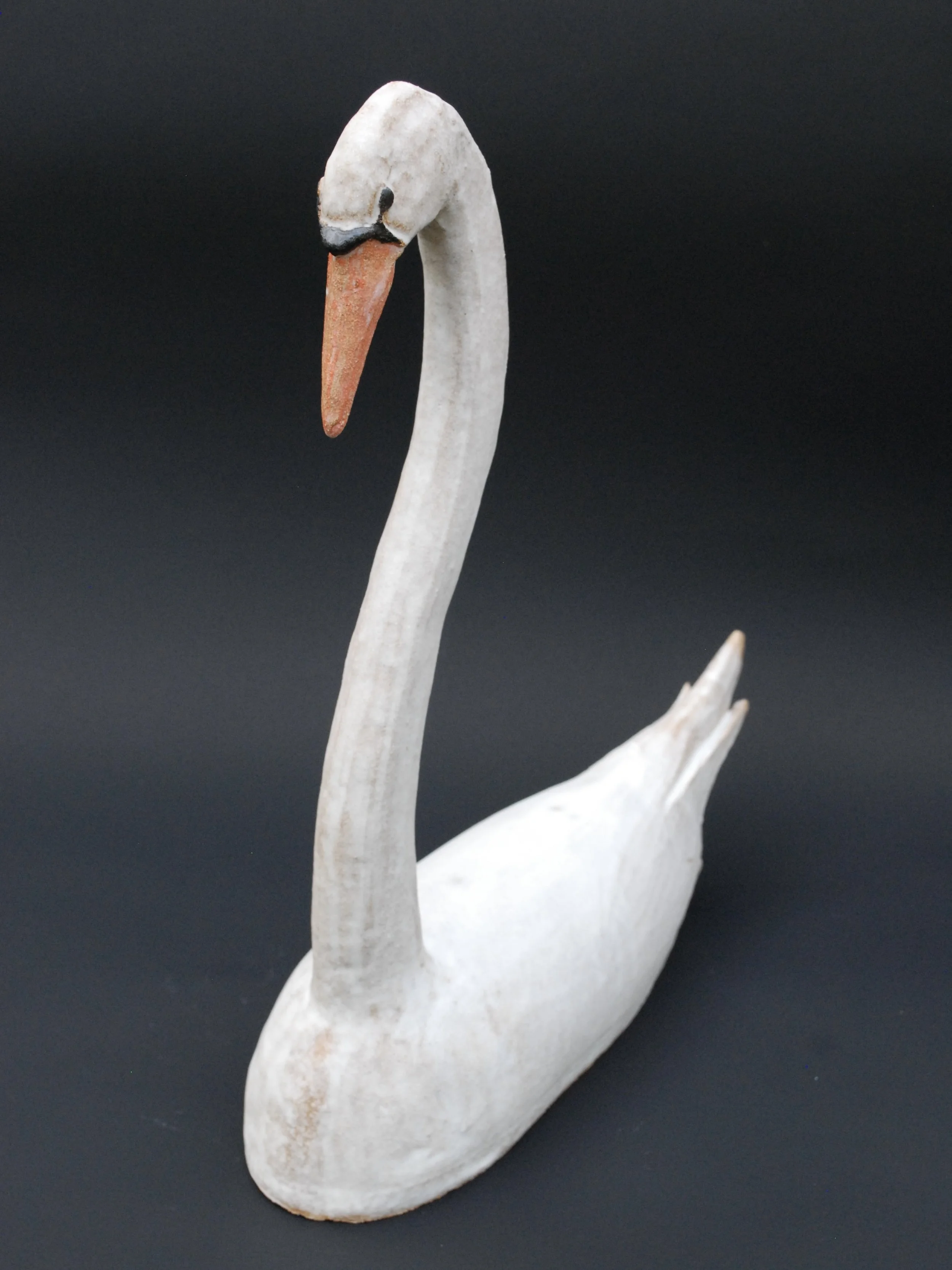 Image shows a large ceramic swan, covered in a white glaze with an orange beak. The swan has an particularly long neck in proportion to its body