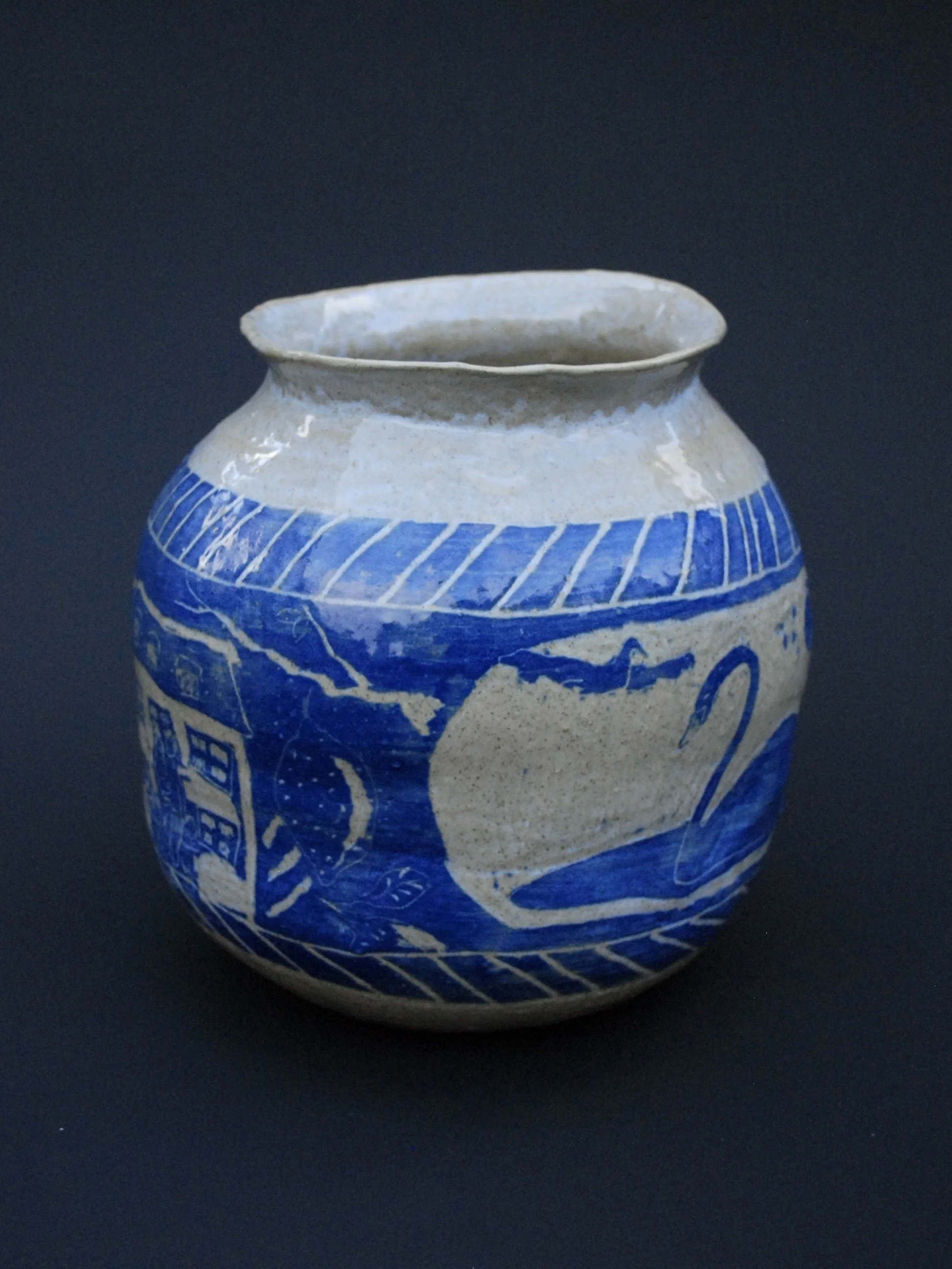 A greek inspired stoneware pot with hand-etched blue designs against a warm, earthy tone. It has a unique and slightly irregular shape adding to the rustic appeal