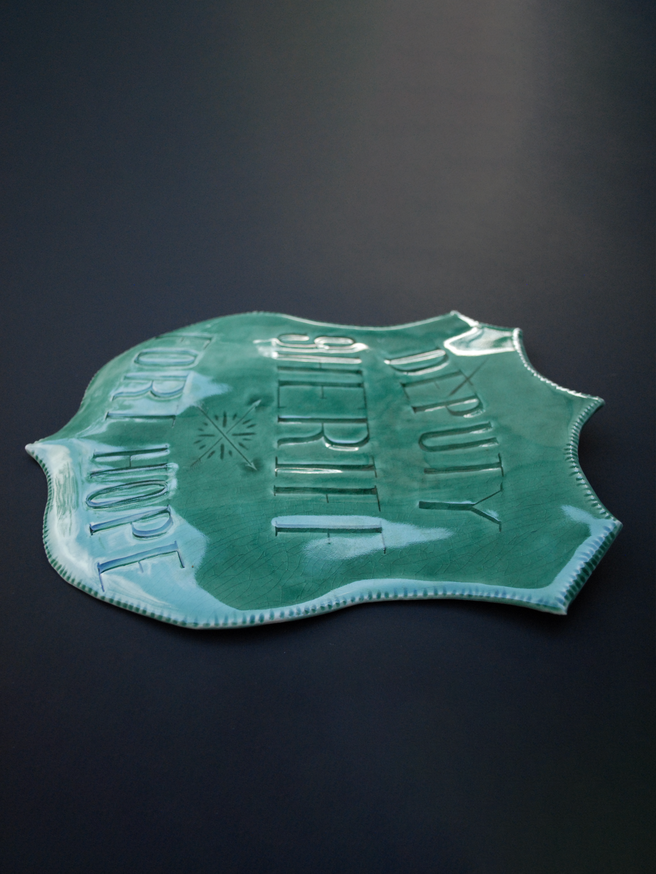 Image shows a large shield shaped badge, with the words 'Deputy Sheriff, Fort hope' etched across. It is finished with a greeny blue crackle glaze finish with a ridged edge.