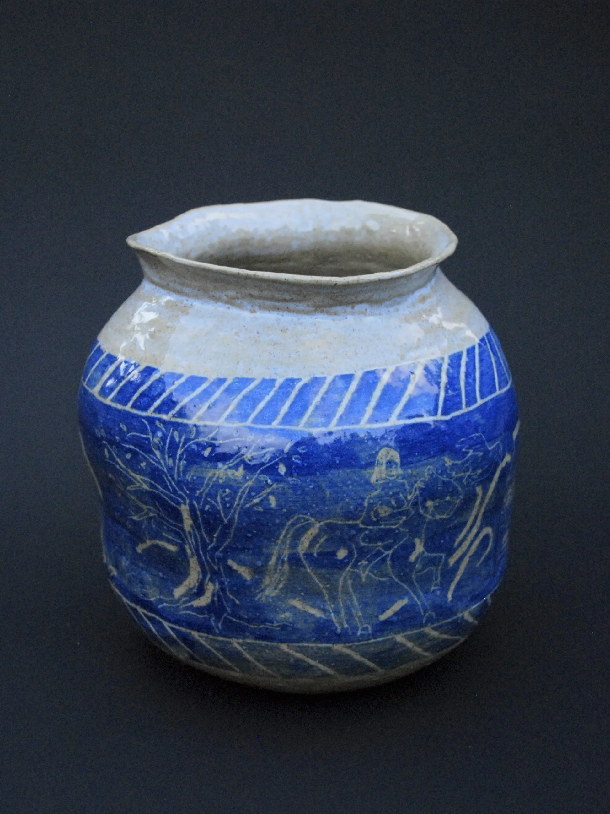 A greek inspired stoneware pot with hand-etched blue designs against a warm, earthy tone. It has a unique and slightly irregular shape adding to the rustic appeal