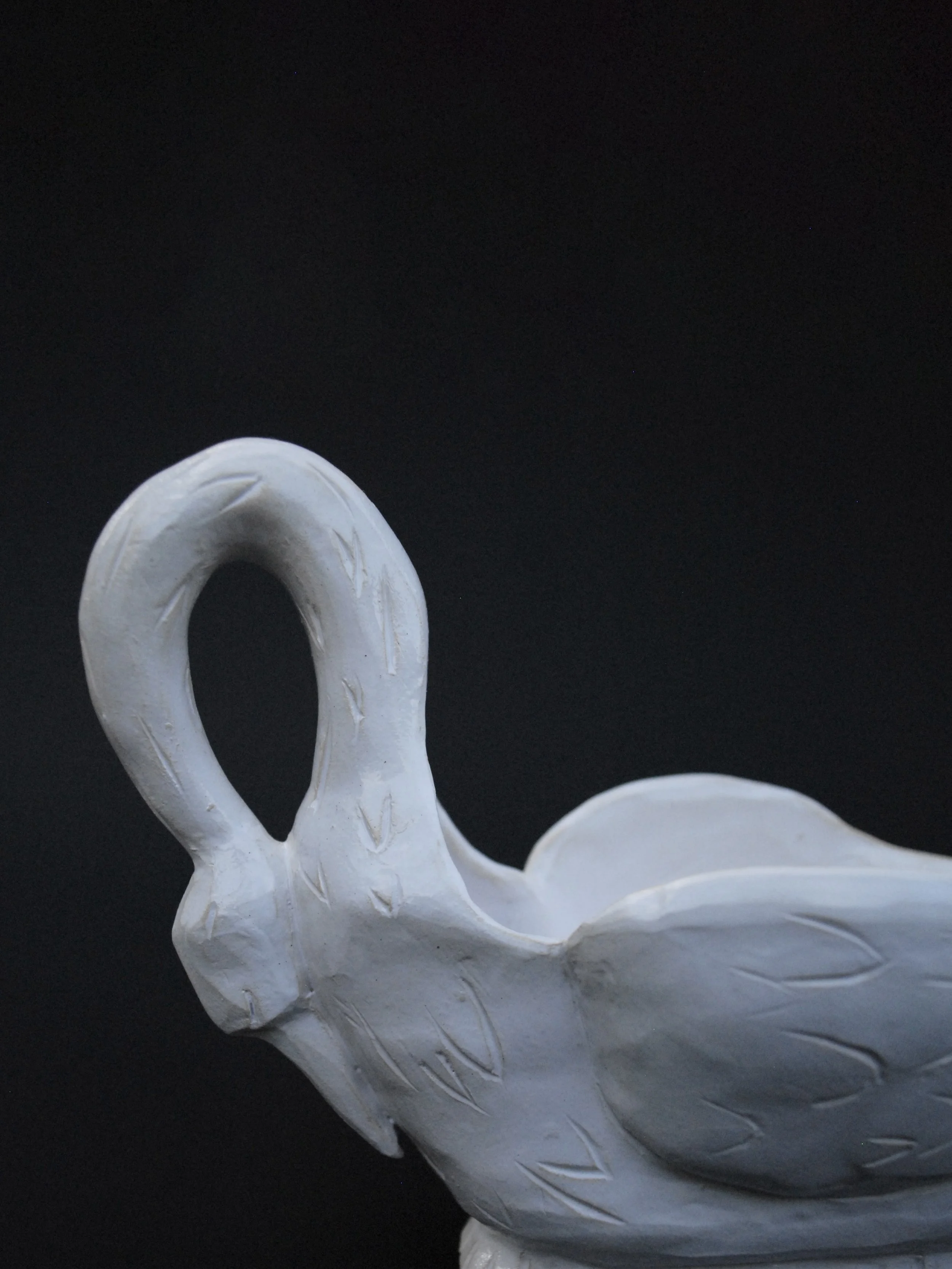 Image shows a ceramic hand-sculpted, swan shaped gravy boat, covered in white glaze and delicate details, it has carved feathers and a long neck which acts as the handle