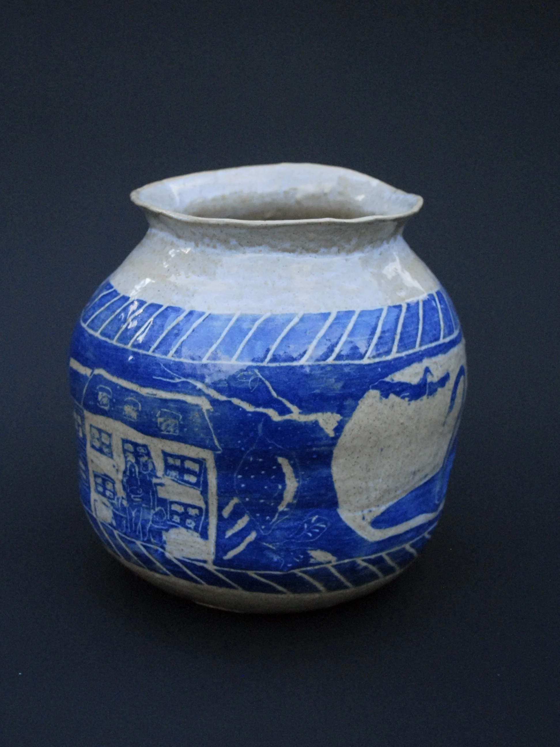 A greek inspired stoneware pot with hand-etched blue designs against a warm, earthy tone. It has a unique and slightly irregular shape adding to the rustic appeal