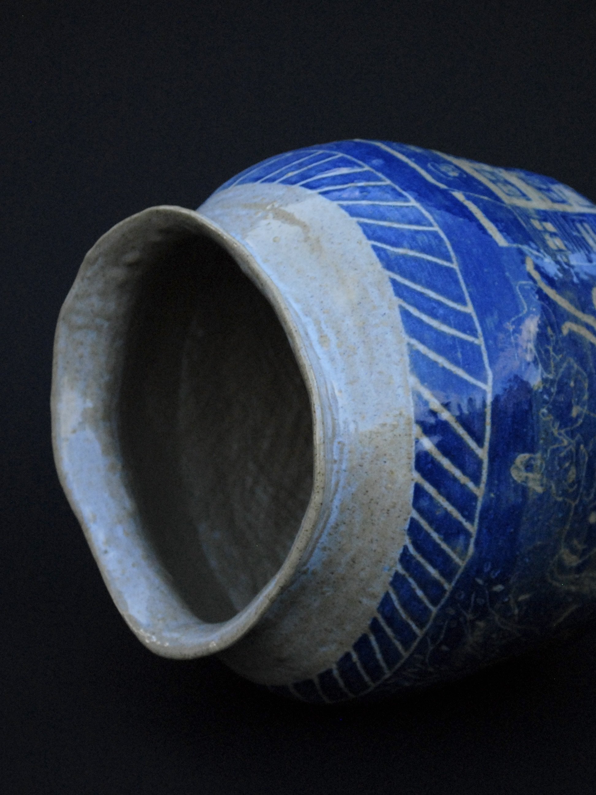 A greek inspired stoneware pot with hand-etched blue designs against a warm, earthy tone. It has a unique and slightly irregular shape adding to the rustic appeal