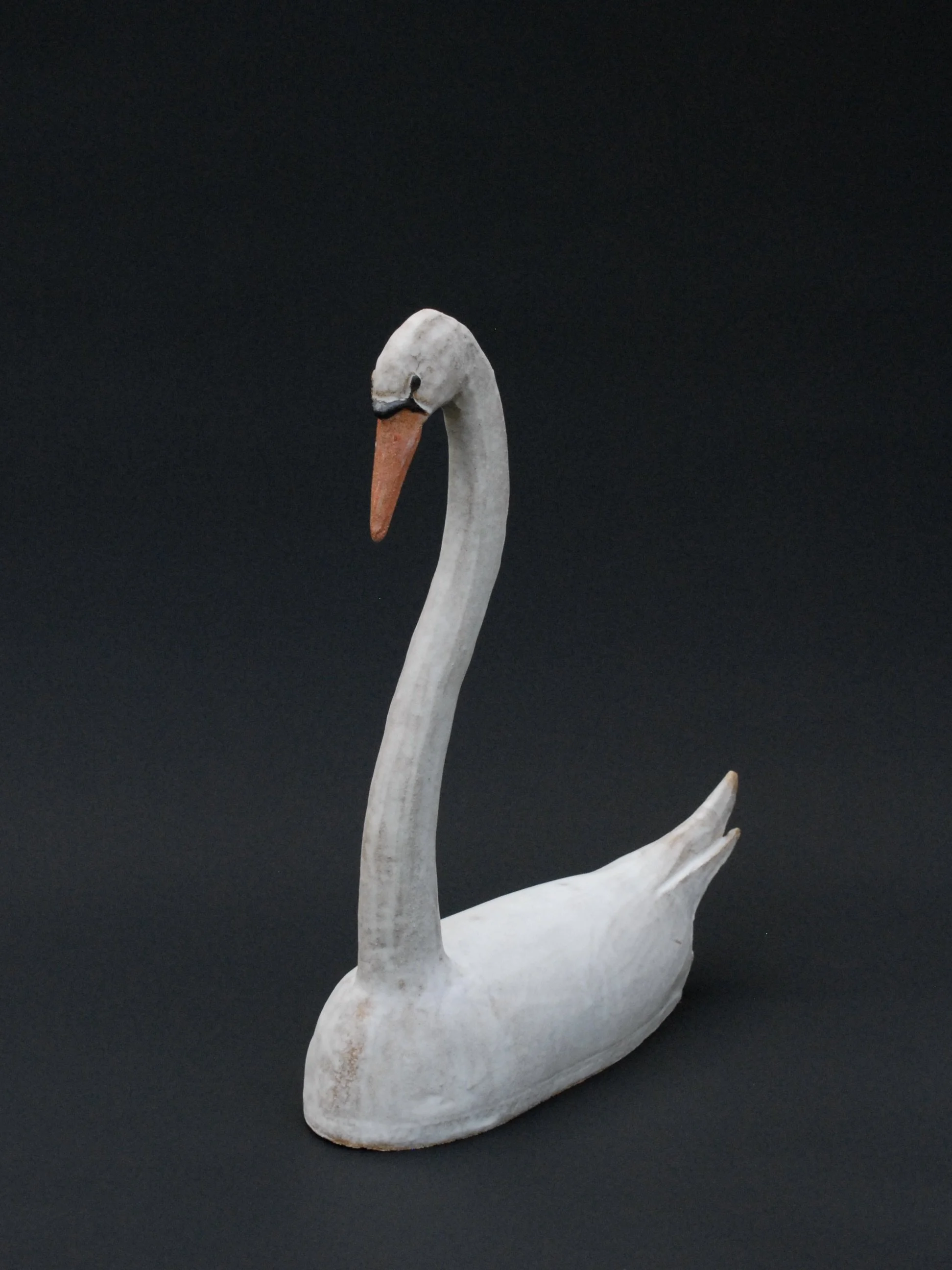 Image shows a large ceramic swan, covered in a white glaze with an orange beak. The swan has an particularly long neck in proportion to its body
