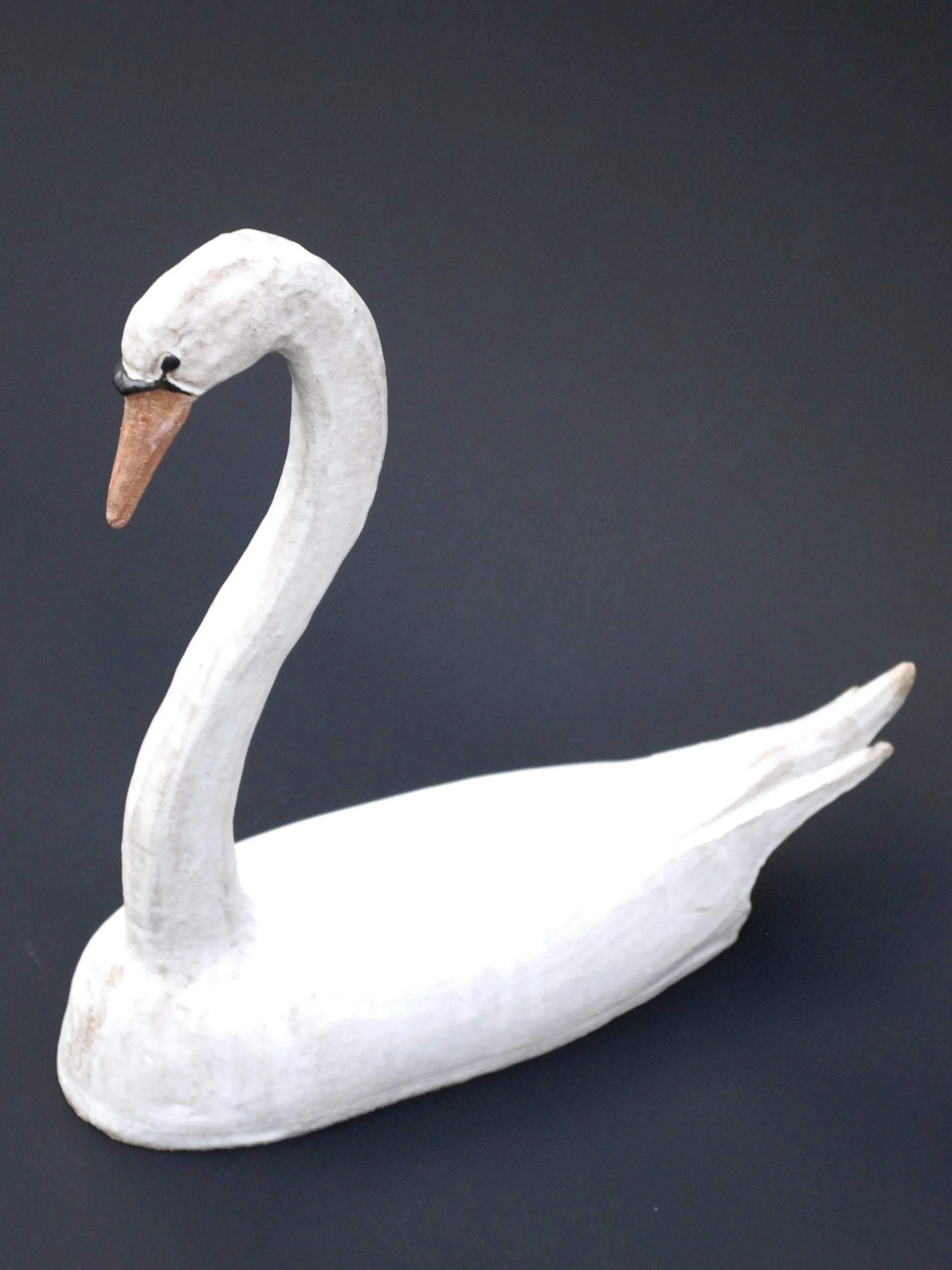 Image shows a large ceramic swan, covered in a white glaze with an orange beak. The swan has an particularly long neck in proportion to its body