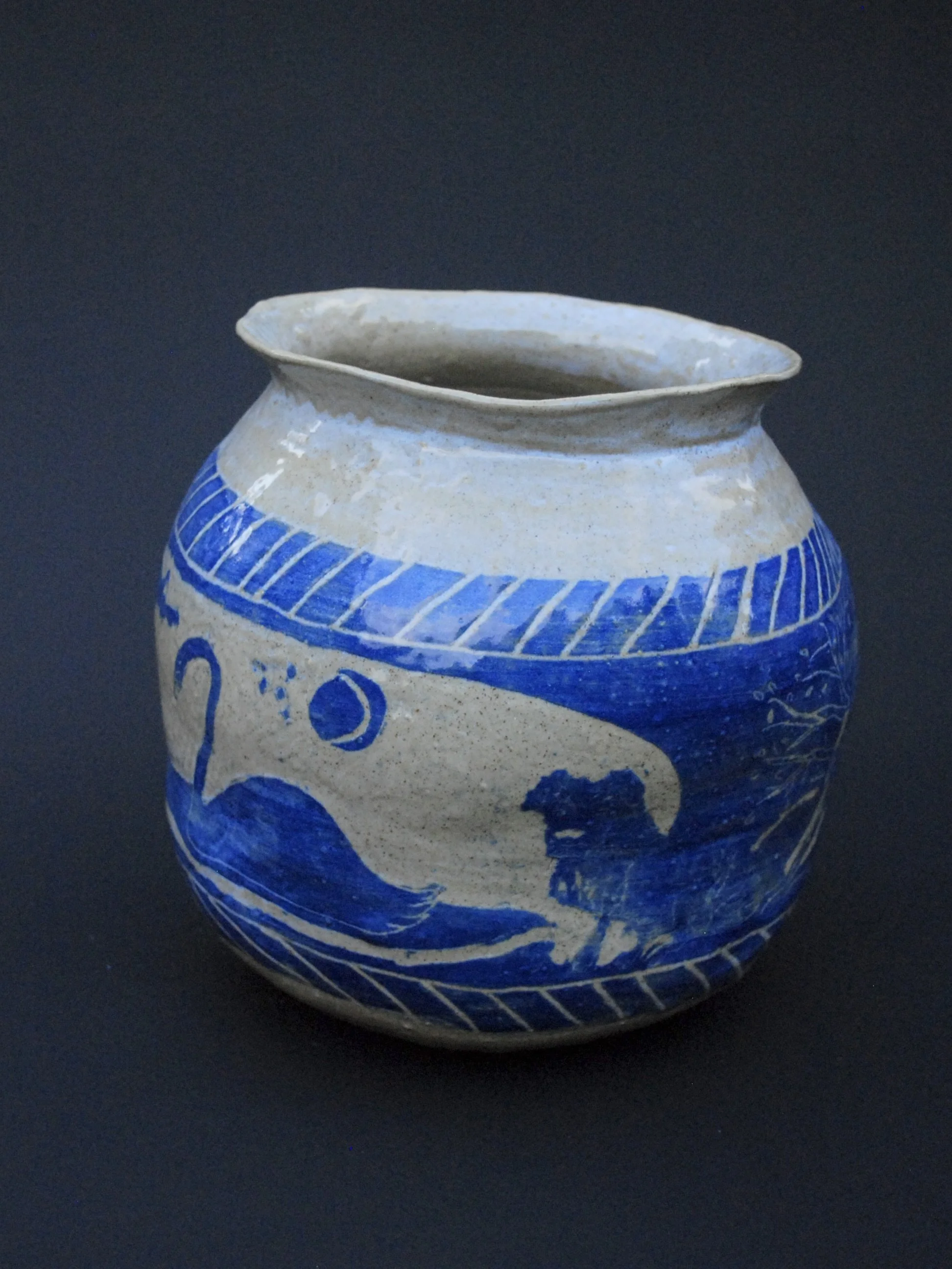 A greek inspired stoneware pot with hand-etched blue designs against a warm, earthy tone. It has a unique and slightly irregular shape adding to the rustic appeal