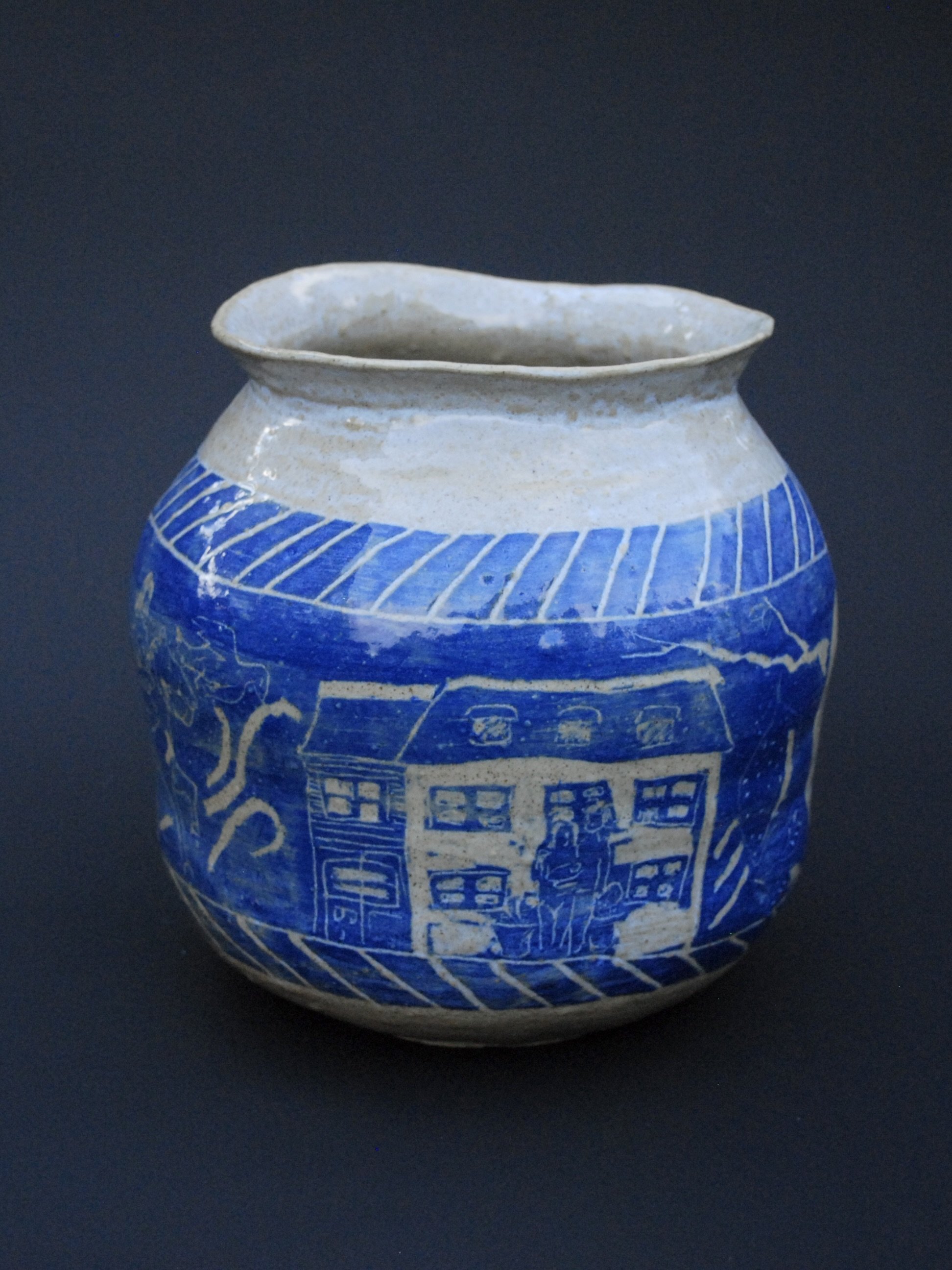 A greek inspired stoneware pot with hand-etched blue designs against a warm, earthy tone. It has a unique and slightly irregular shape adding to the rustic appeal