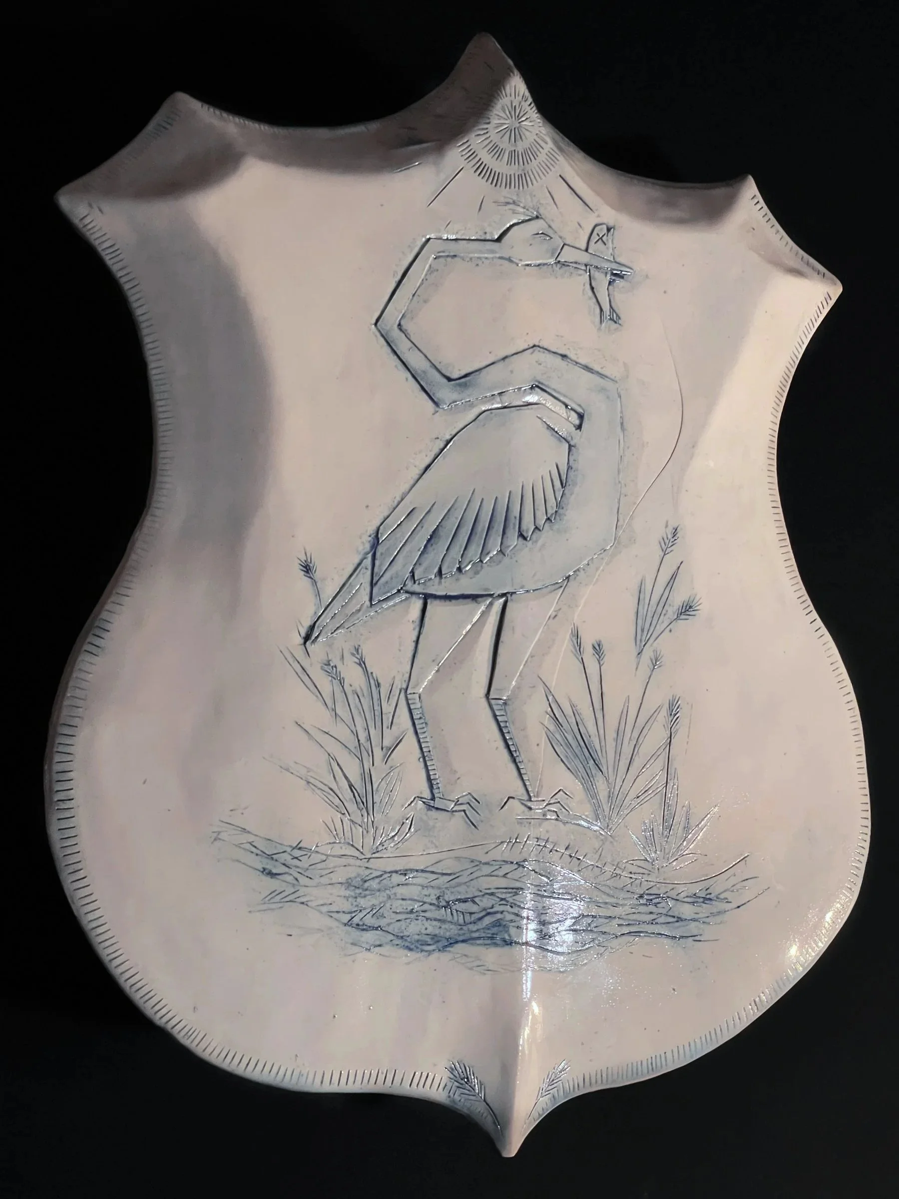The Crane, white ceramic shield-shaped wall piece with a crane holding a fish among reeds, carved in cobalt blue