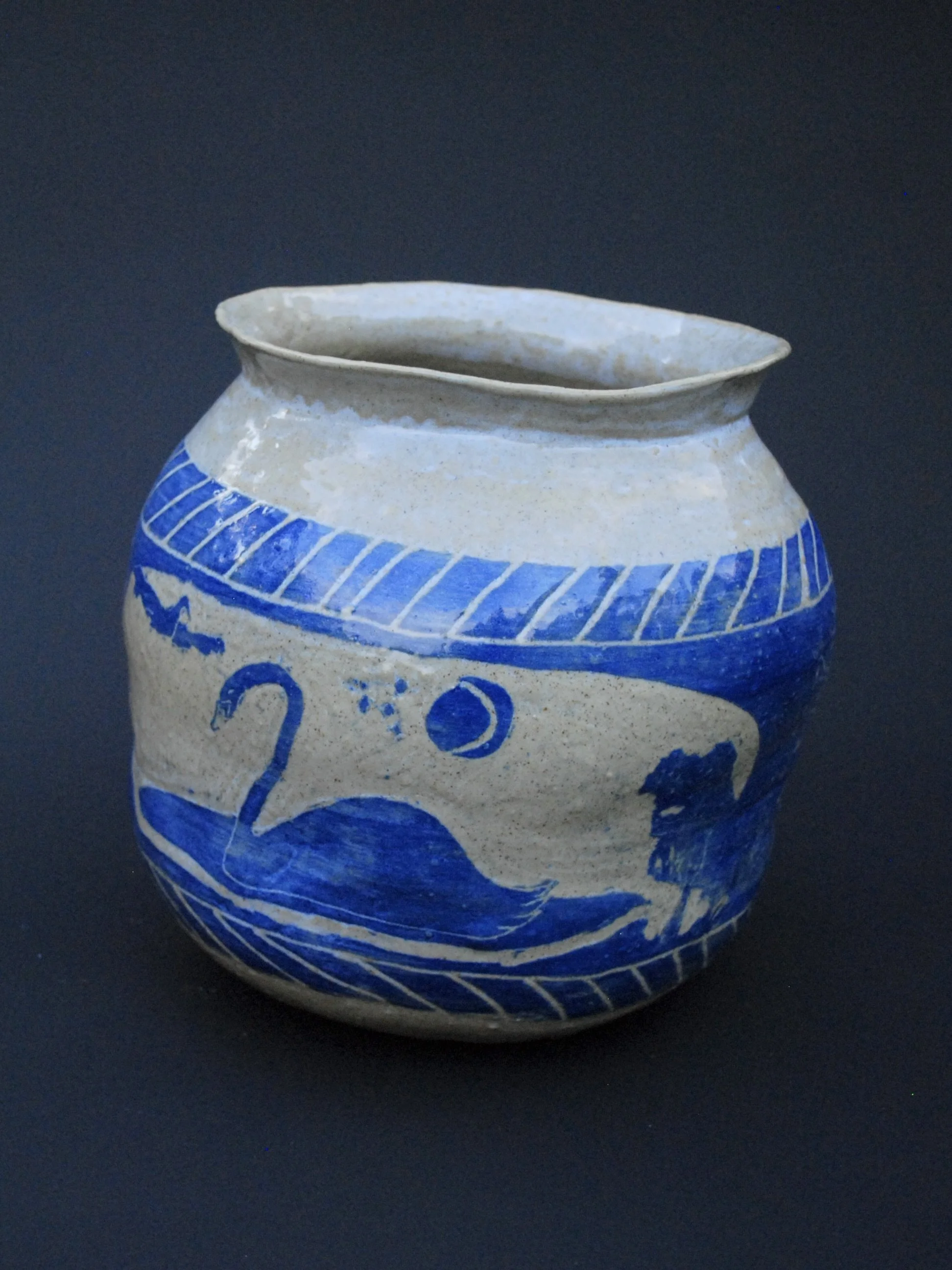 A greek inspired stoneware pot with hand-etched blue designs against a warm, earthy tone. It has a unique and slightly irregular shape adding to the rustic appeal