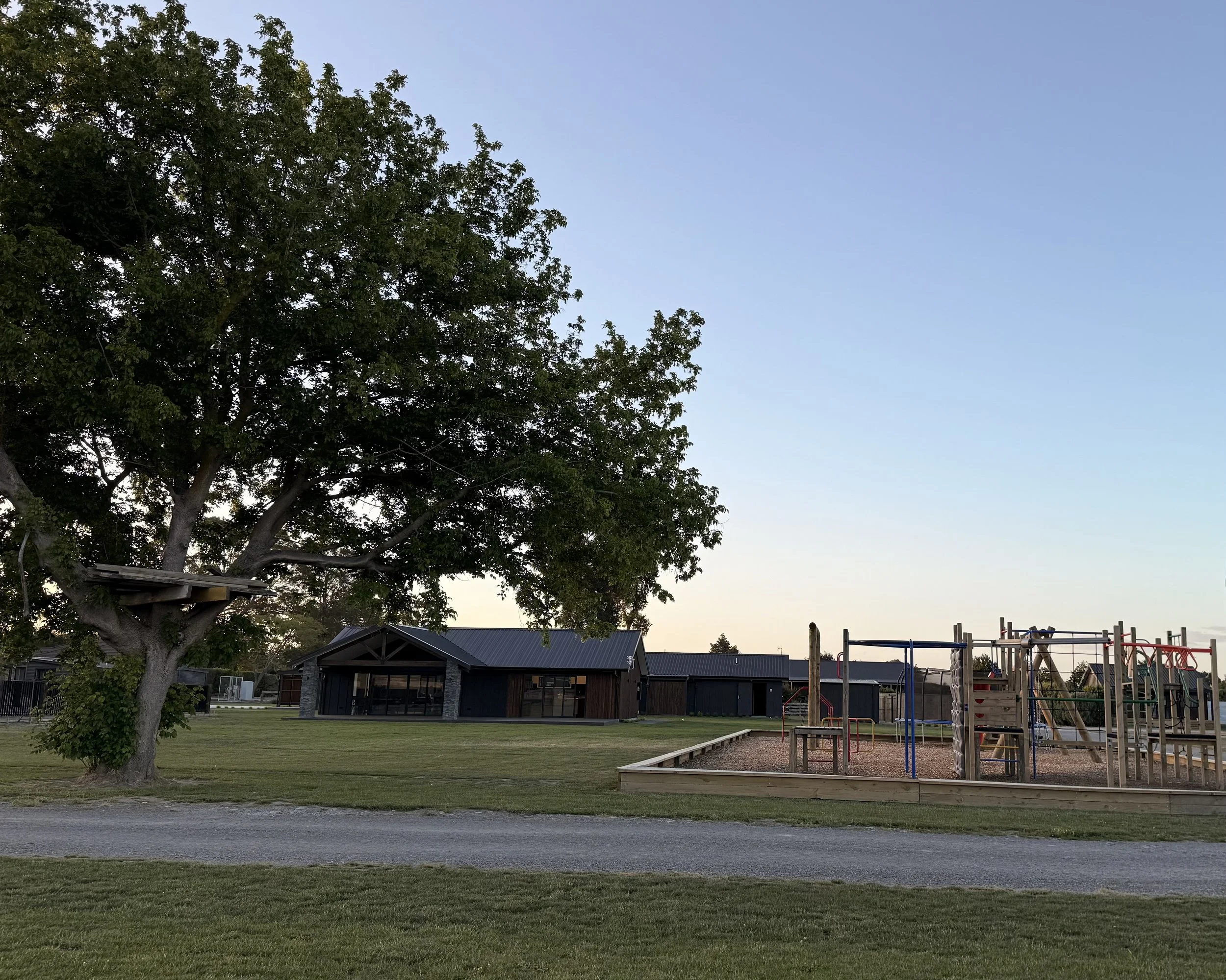 A playground with climbing structures and a large tree in the background during dusk.