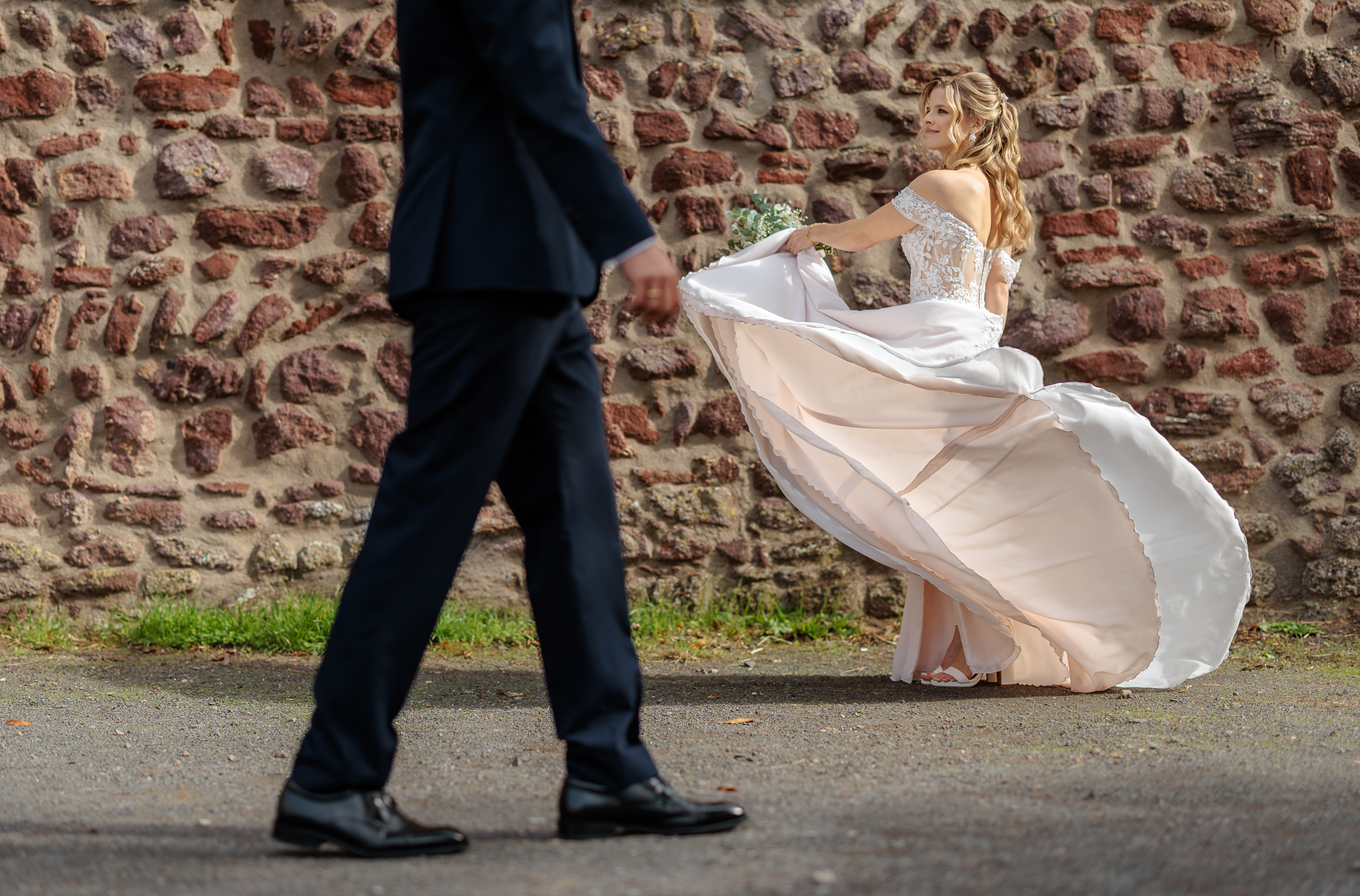 Braut in einem weißen Hochzeitskleid tanzt vor einer alten Steinmauer auf Burg Hayn, während ein Bräutigam in einem dunklen Anzug im Vordergrund tanzt.
